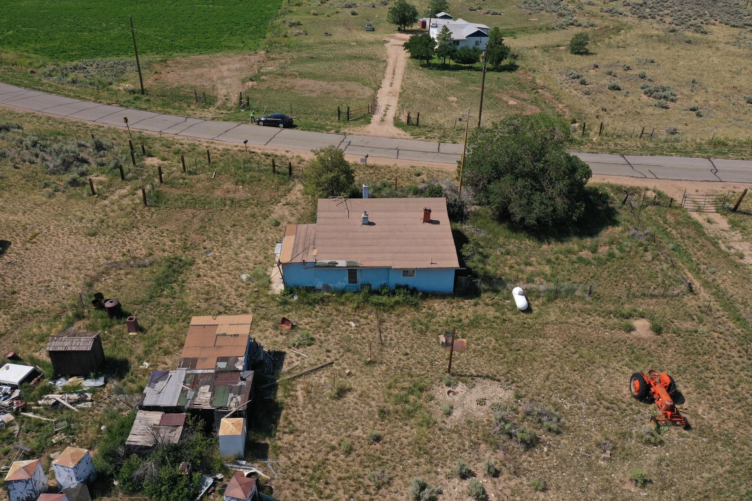 Aerial view of a rural property with houses, dirt and paved roads, trees, fencing, and agricultural equipment in a semi-arid landscape.
