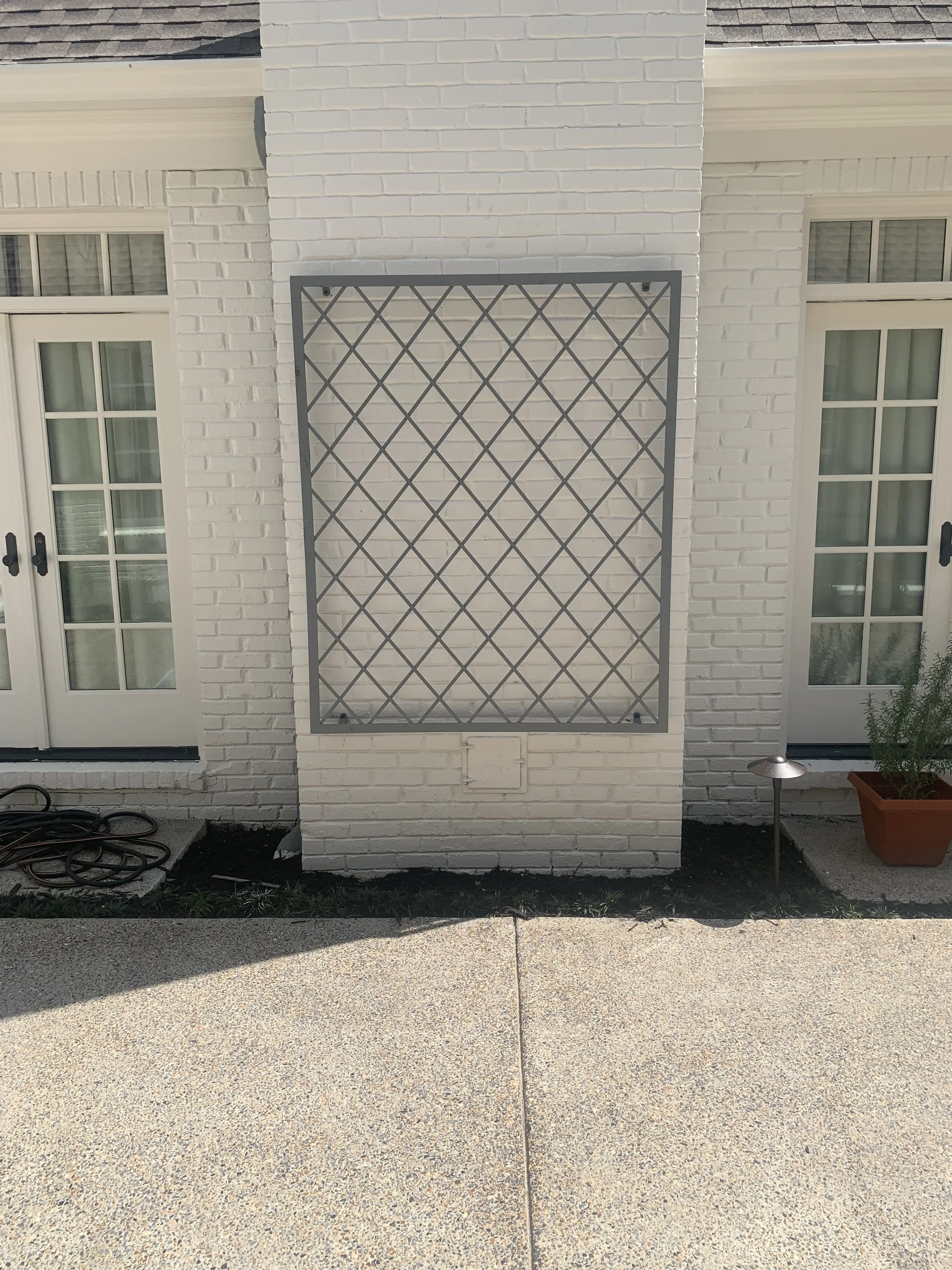 White brick house with double glass doors, window boxes with plants, and a metal ladder frame on the wall.