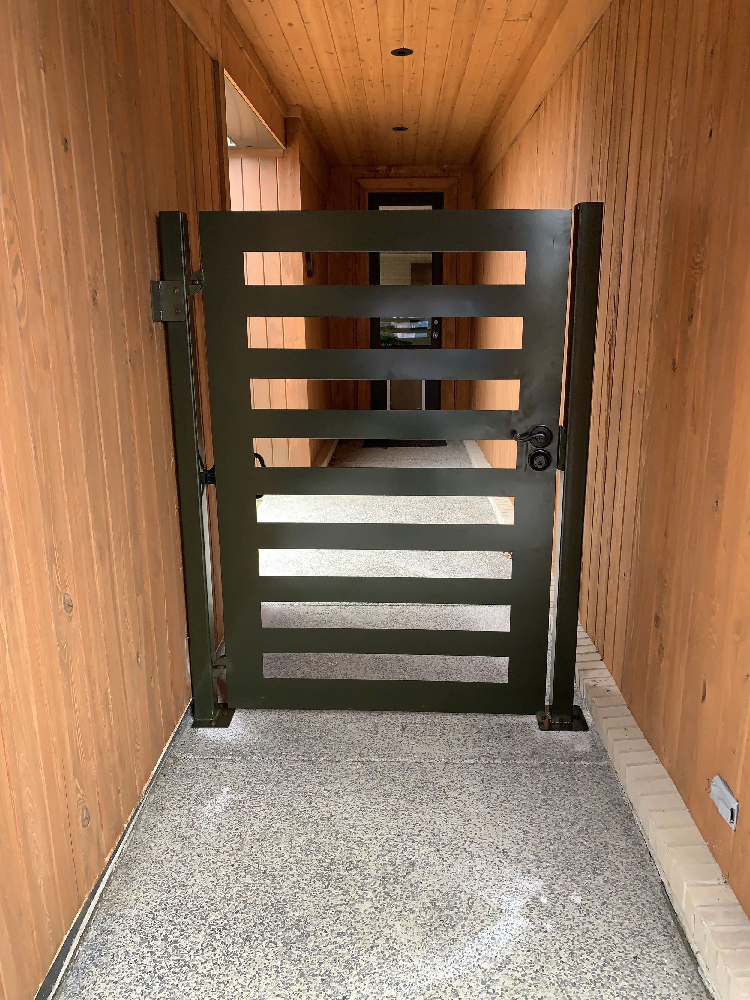 Green metal security gate in a wooden hallway.