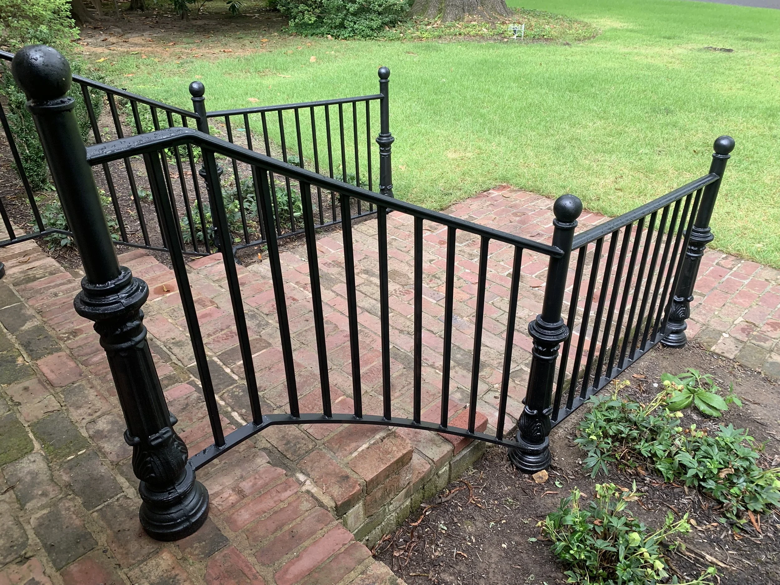 A black metal fence around a small brick patio on a garden lawn.