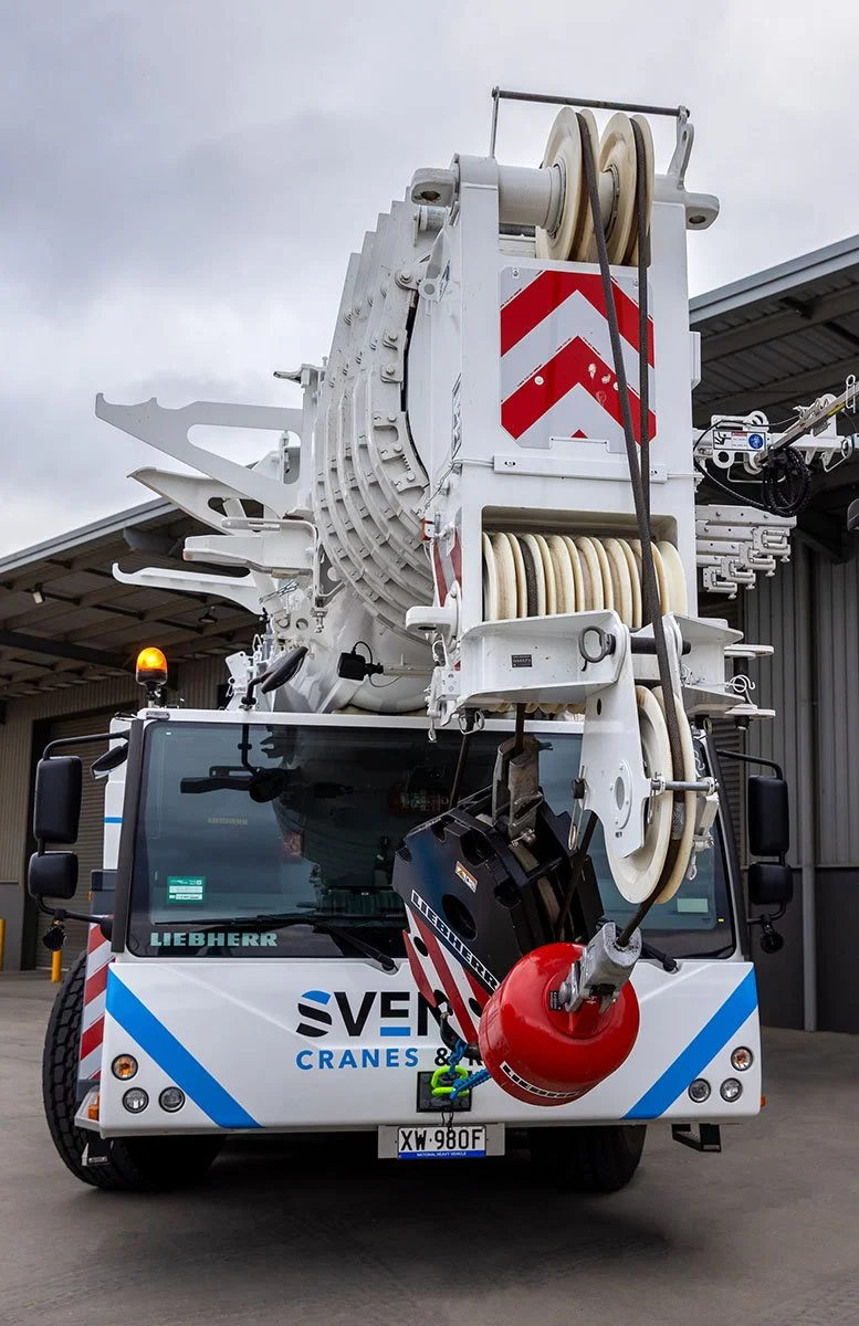 250 tonne mobile crane with the brand 'Sventek' on it, lifting construction materials at a building site under a blue sky with clouds.