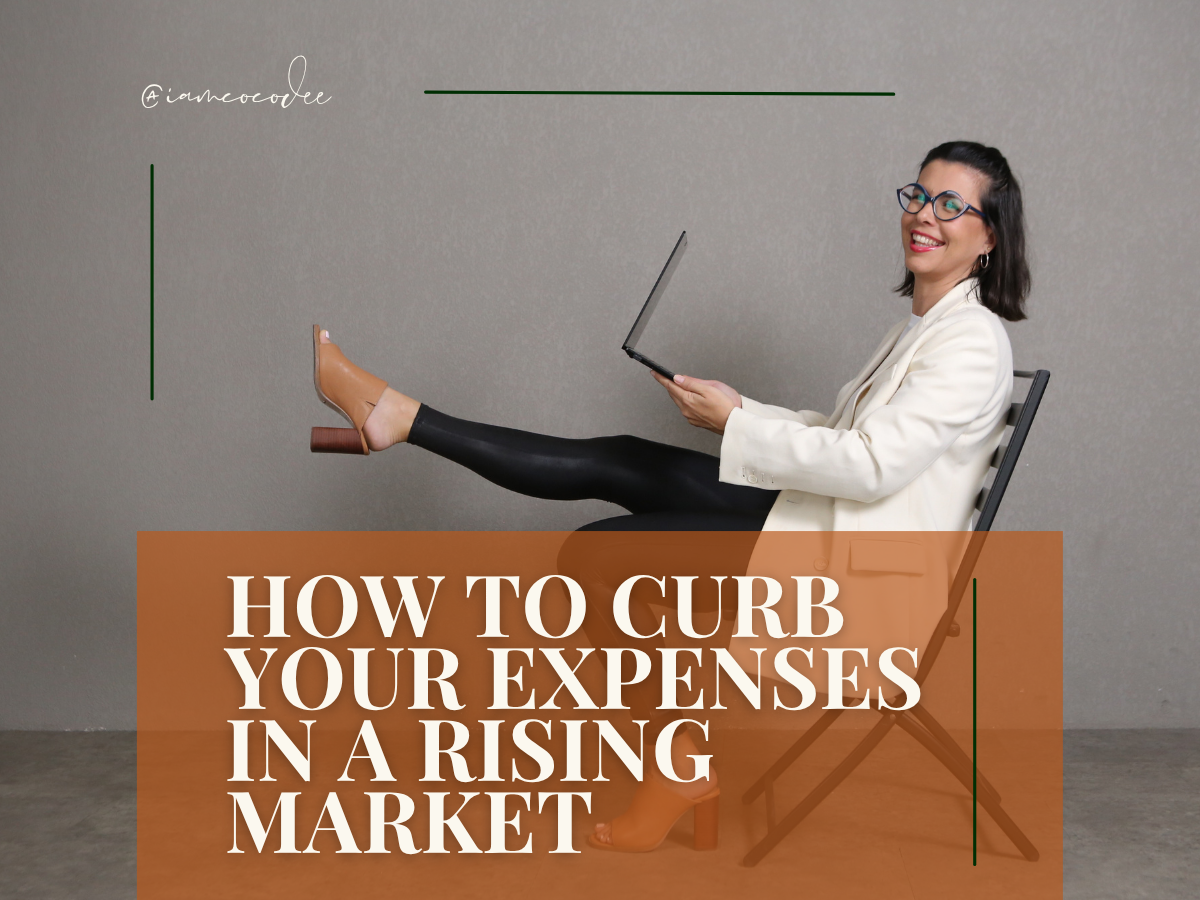 A woman with black hair, glasses, white blazer, and black leather pants sitting on a chair, smiling while holding a laptop. There is a text overlay that reads, "HOW TO CURB YOUR EXPENSES IN A RISING MARKET" and a handwritten text that says "@iamcocoe" on a plain gray background.