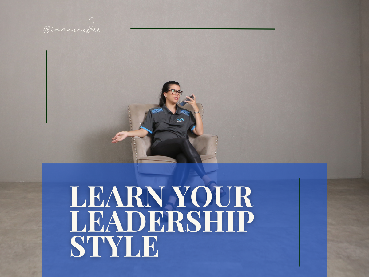 A woman sitting on a beige armchair against a plain wall, wearing a dark shirt and glasses, holding a phone. Overlaid text reads 'Learn Your Leadership Style' in white on a blue background.