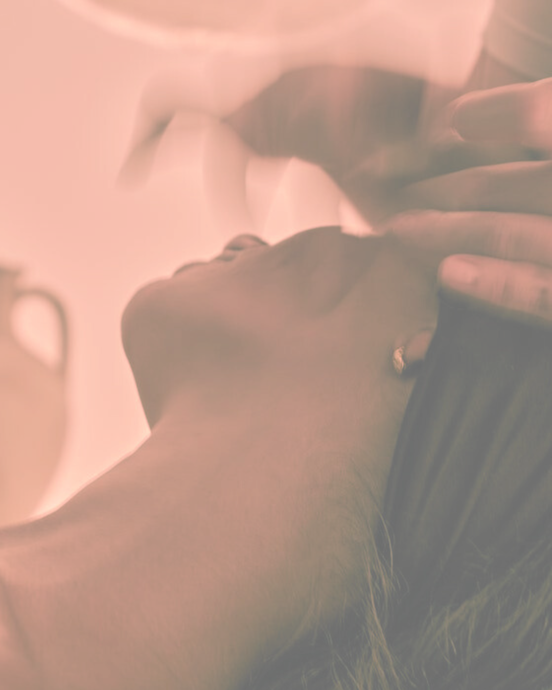 Close-up of a person lying with their head tilted back and hand gently touching their face, soft pink lighting.
