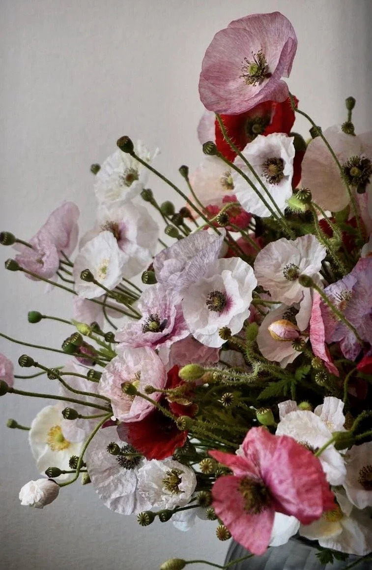 Un bouquet de fleurs, principalement des coquelicots roses, blancs et rouges, dans un vase.
