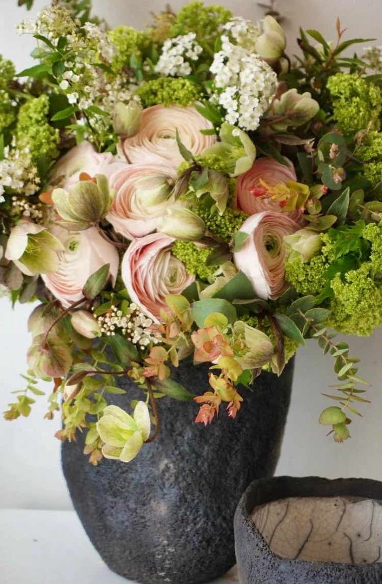 Un arrangement floral avec des roses, hortensias, et autres fleurs dans un vase noir en céramique.