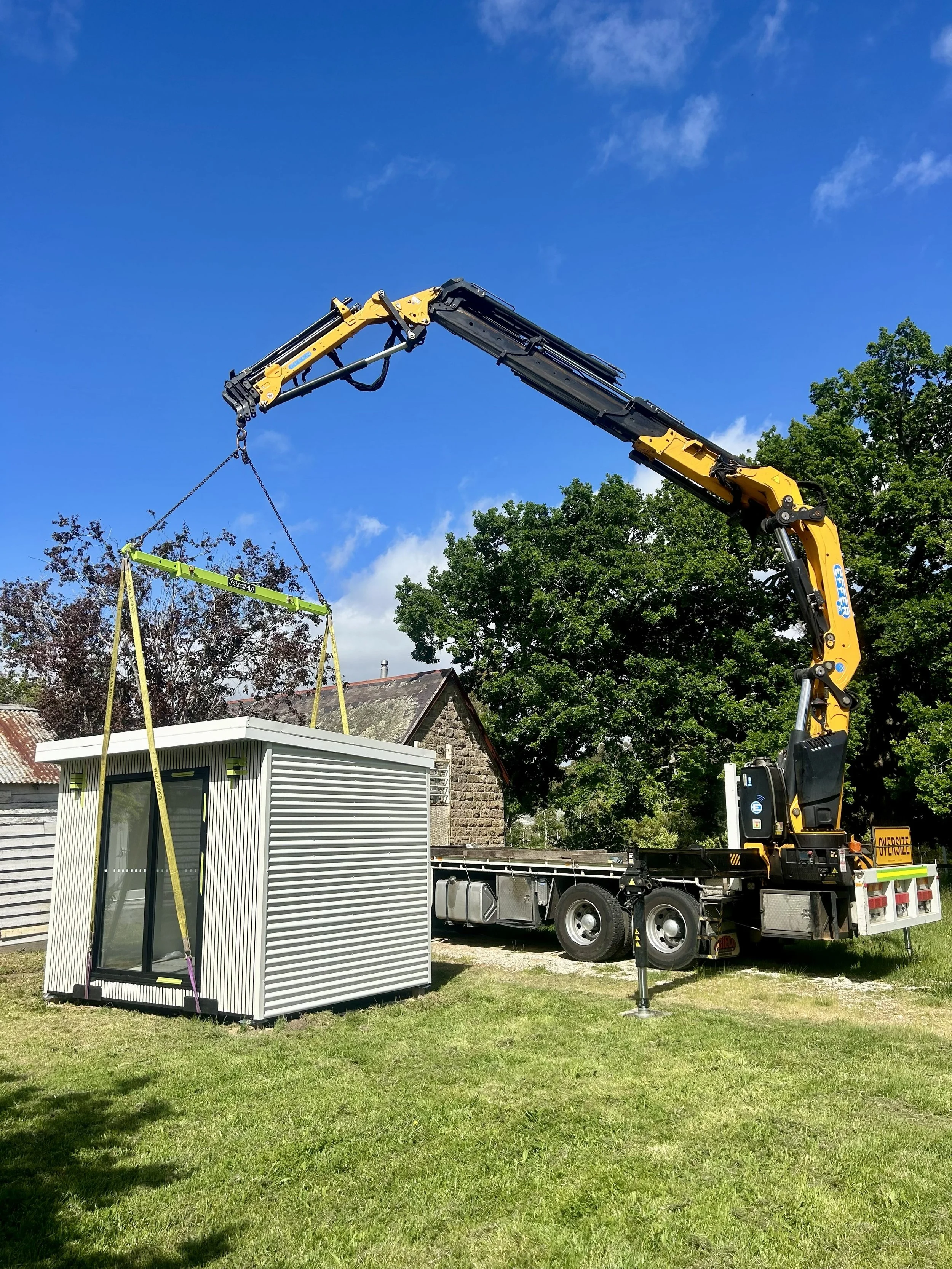 Cope Crane Truck's extended Effer truck-mounted crane lowering a tiny home down in a backyard.. The image is used as an example of Cope Crane Truck's crane truck hire services for portable buildings..