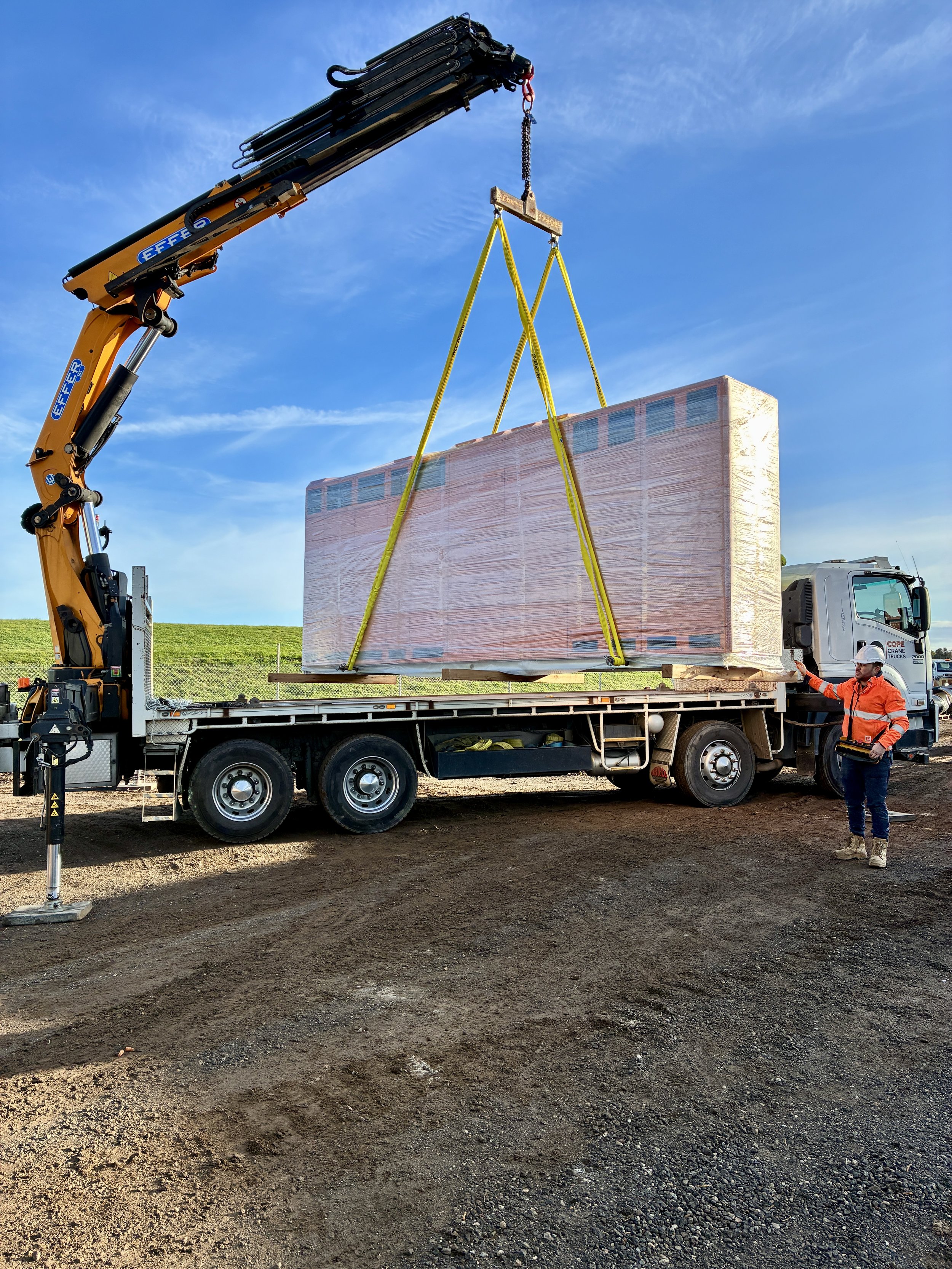 Anthony Cope guiding a large piece of machinery off the crane truck bed with the use of the Effer truck mounted crane.. The image is used as an example of Cope Crane Truck's crane truck hire project management service.