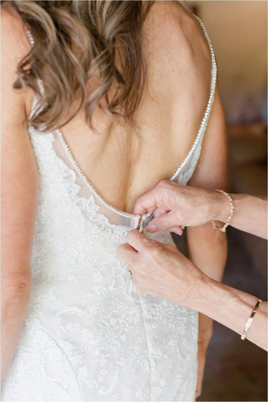 Mother of the bride buttons the bride's wedding gown