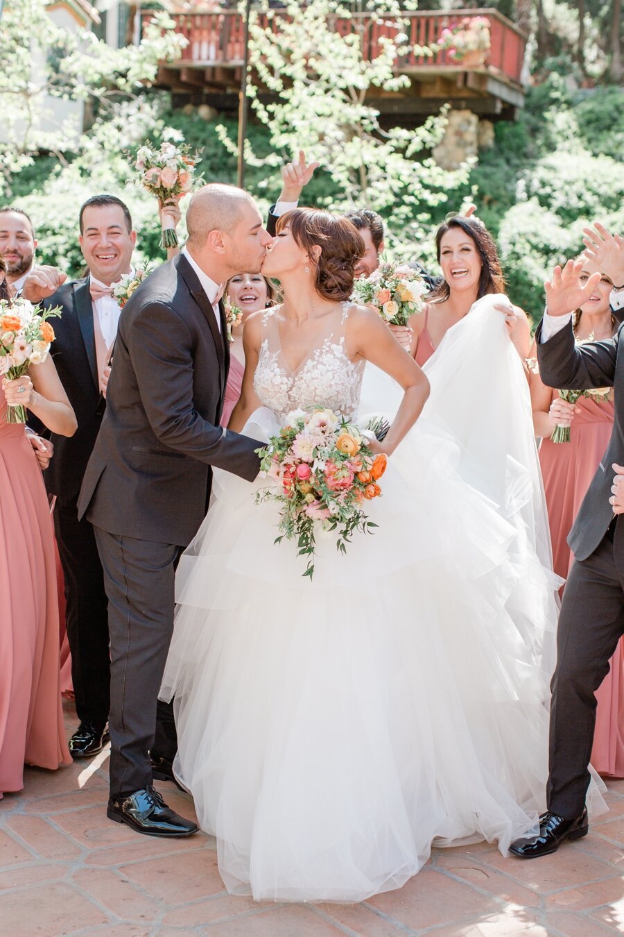 bride and groom kiss while wedding party cheers