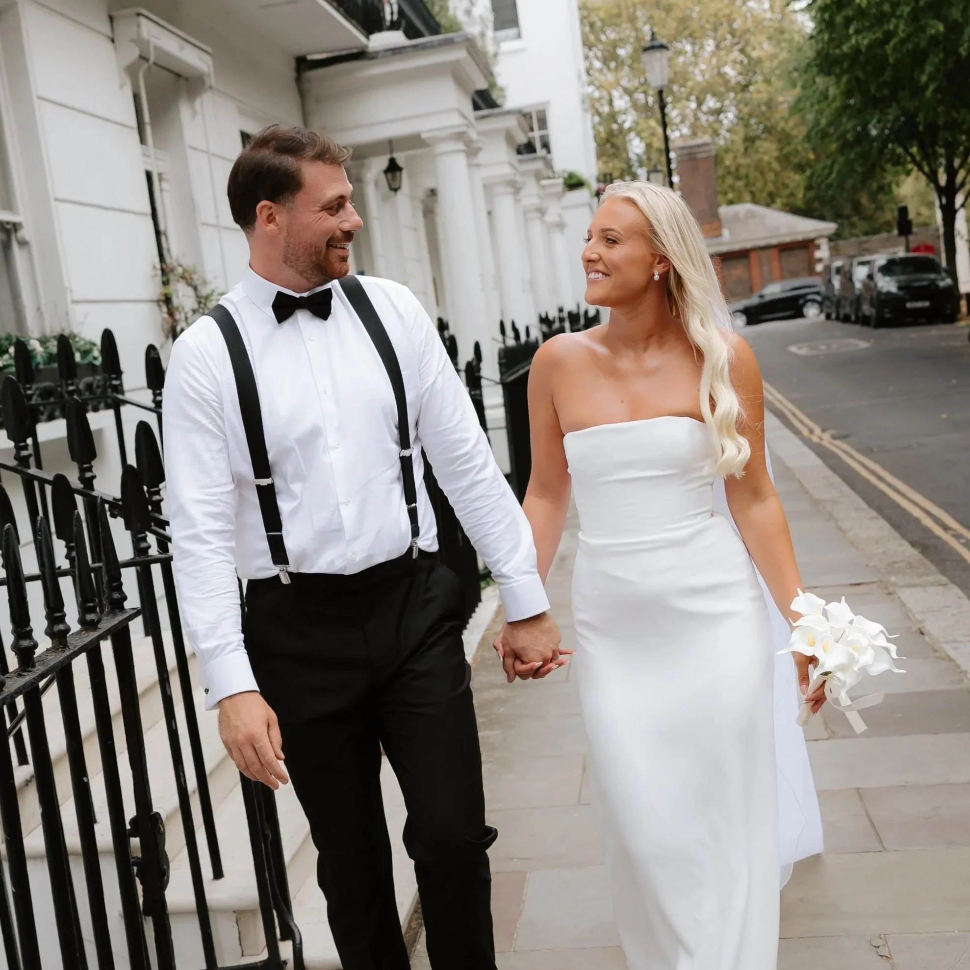 Newly married couple walking down London Street holding hands wearing wedding dress and Tuxedo