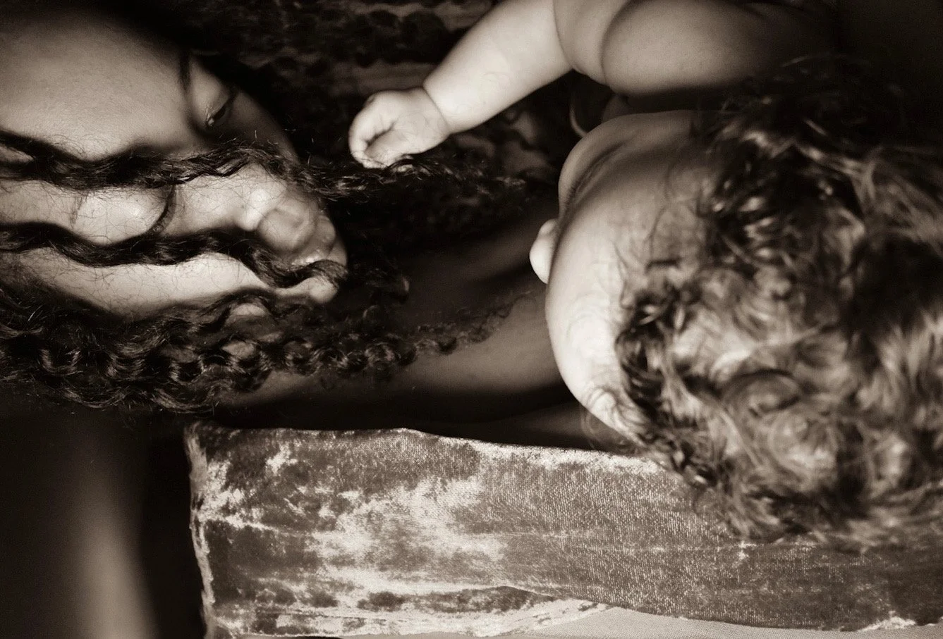 Due persone, un adulto e un bambino, con i capelli ricci, visti di lato, in un momento intimo e affettuoso, in tonalità di sepia.