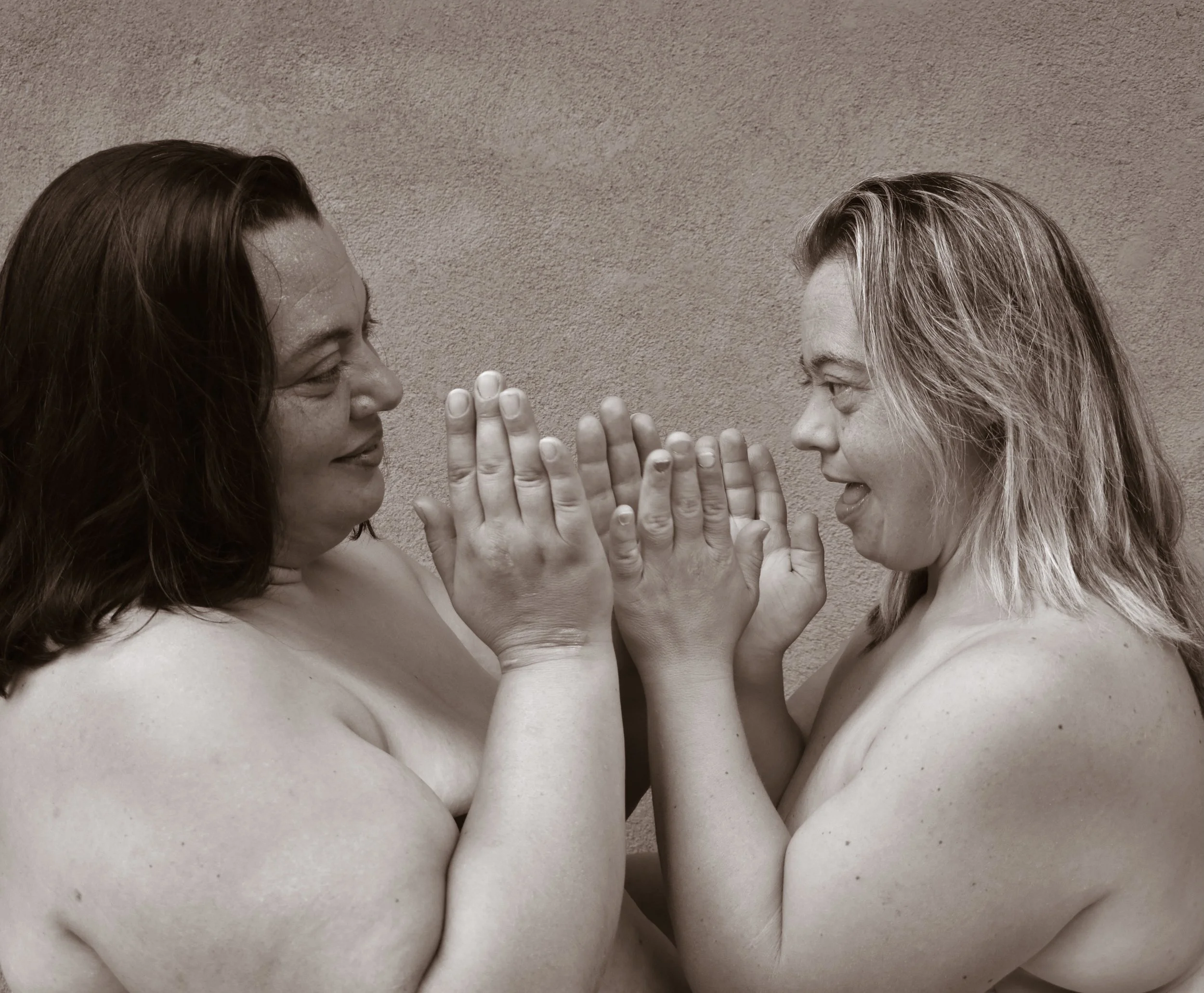Due donne nude si sorridono e si avvicinano con le mani toccandosi le palme, in un'immagine in bianco e nero.