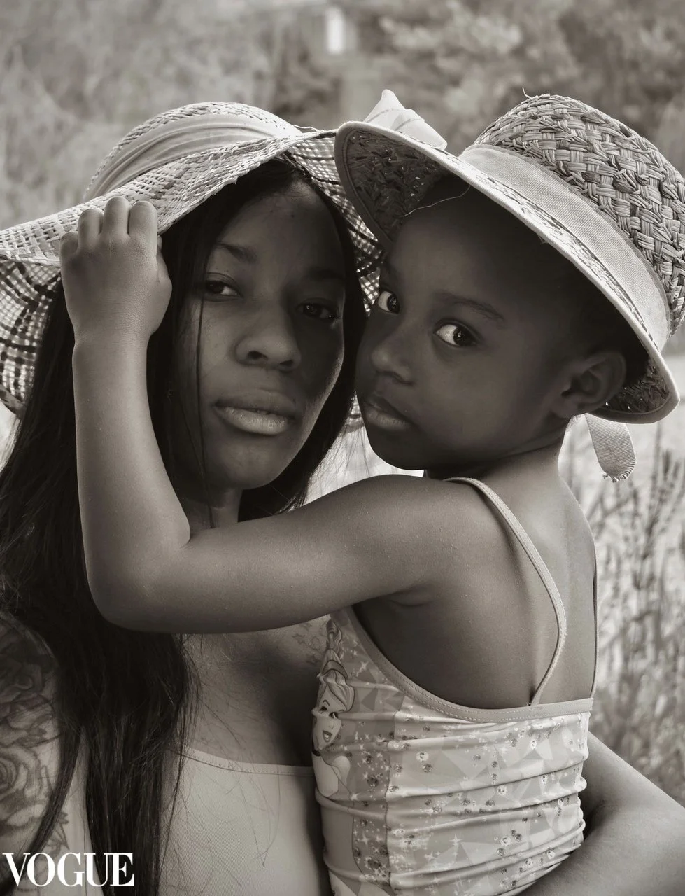 Una donna e una bambina in abbigliamento estivo indossano cappelli di paglia, si abbracciano e guardano l'obiettivo, in un ambiente naturale.