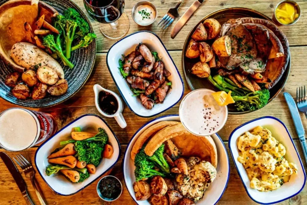 Sunday beef roast dinner on wooden table with sides and real ale