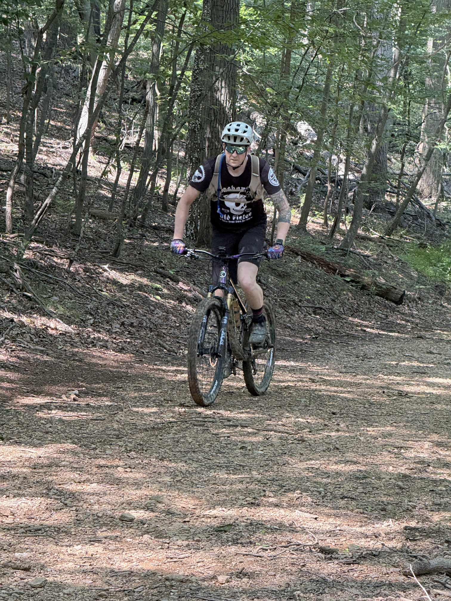 A person mountain biking on a forest trail with trees and uneven terrain.