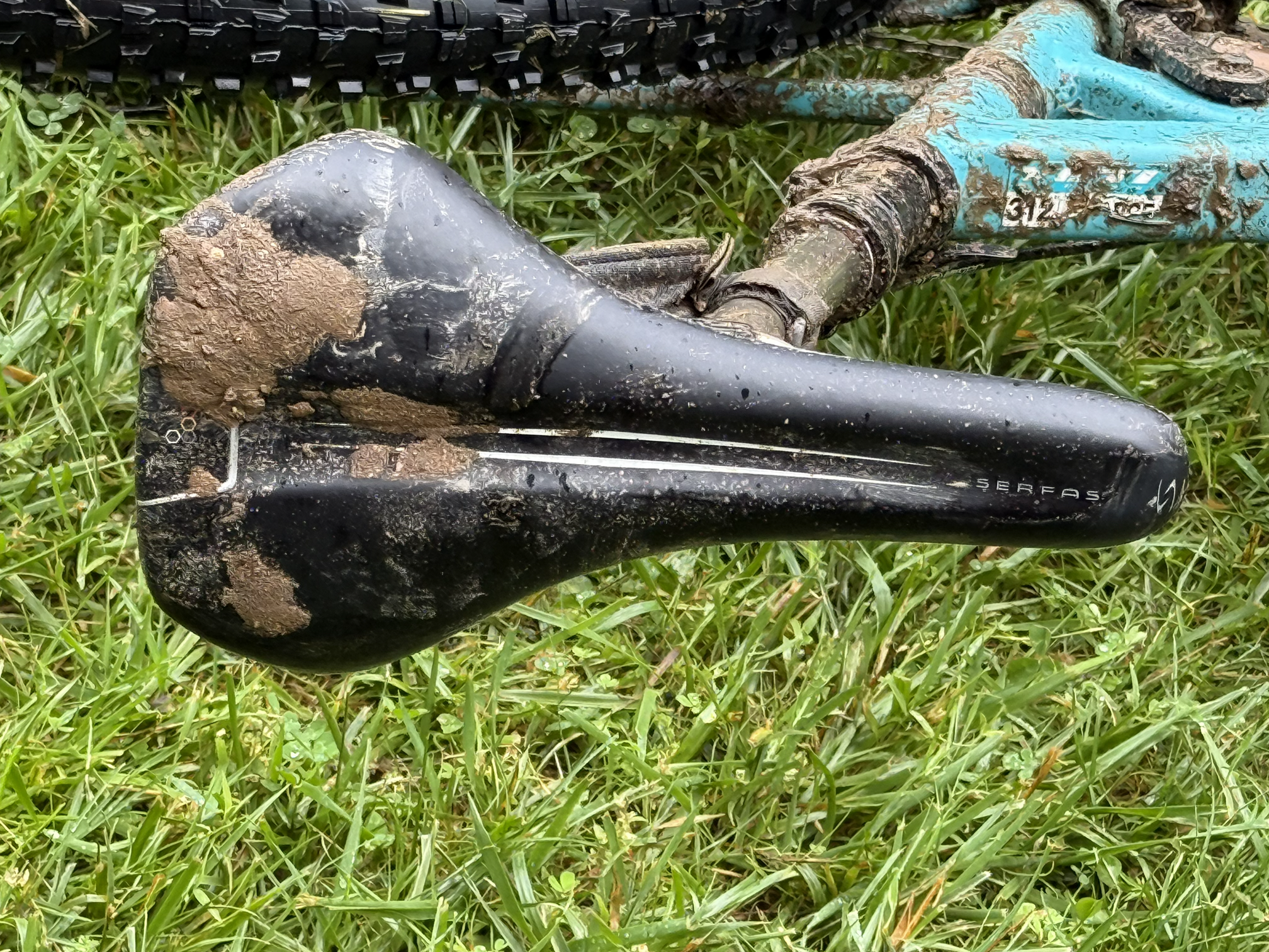 Muddy and dirty mountain bike lying on grass with a muddy blue frame and black tires.
