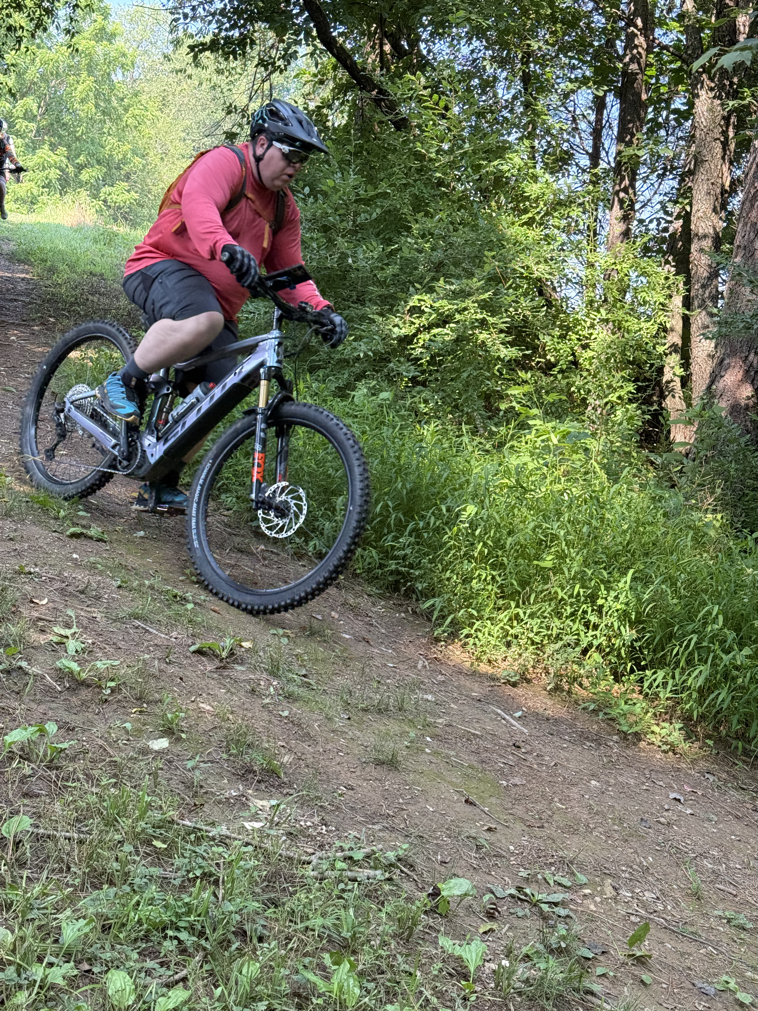 Person riding a mountain bike on a wooded trail, wearing a helmet and red shirt.