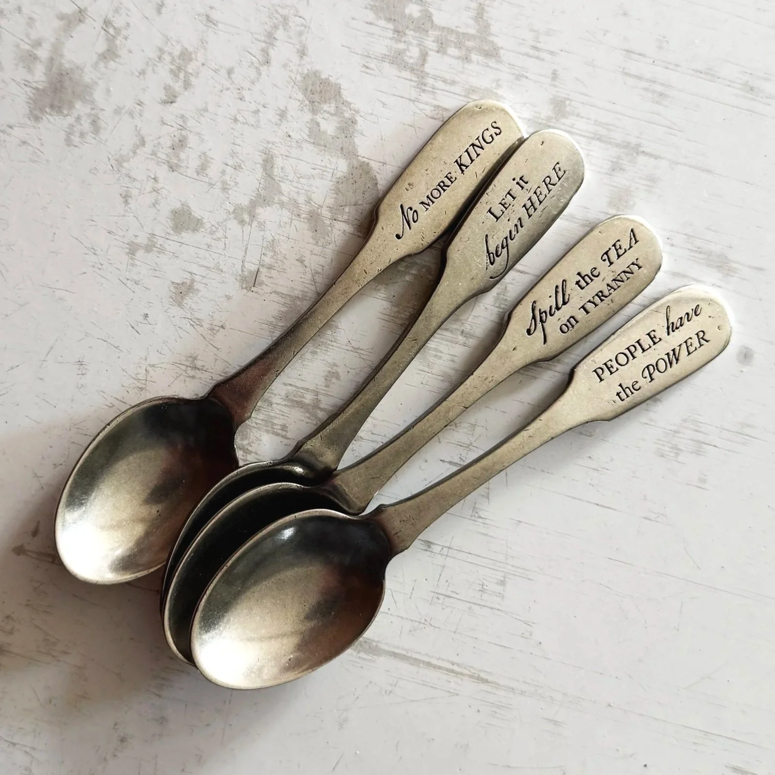 4 pewter spoons engraved with slogans harkening back to the Revolutionary War including "People Have the Power and "No More Kings!"