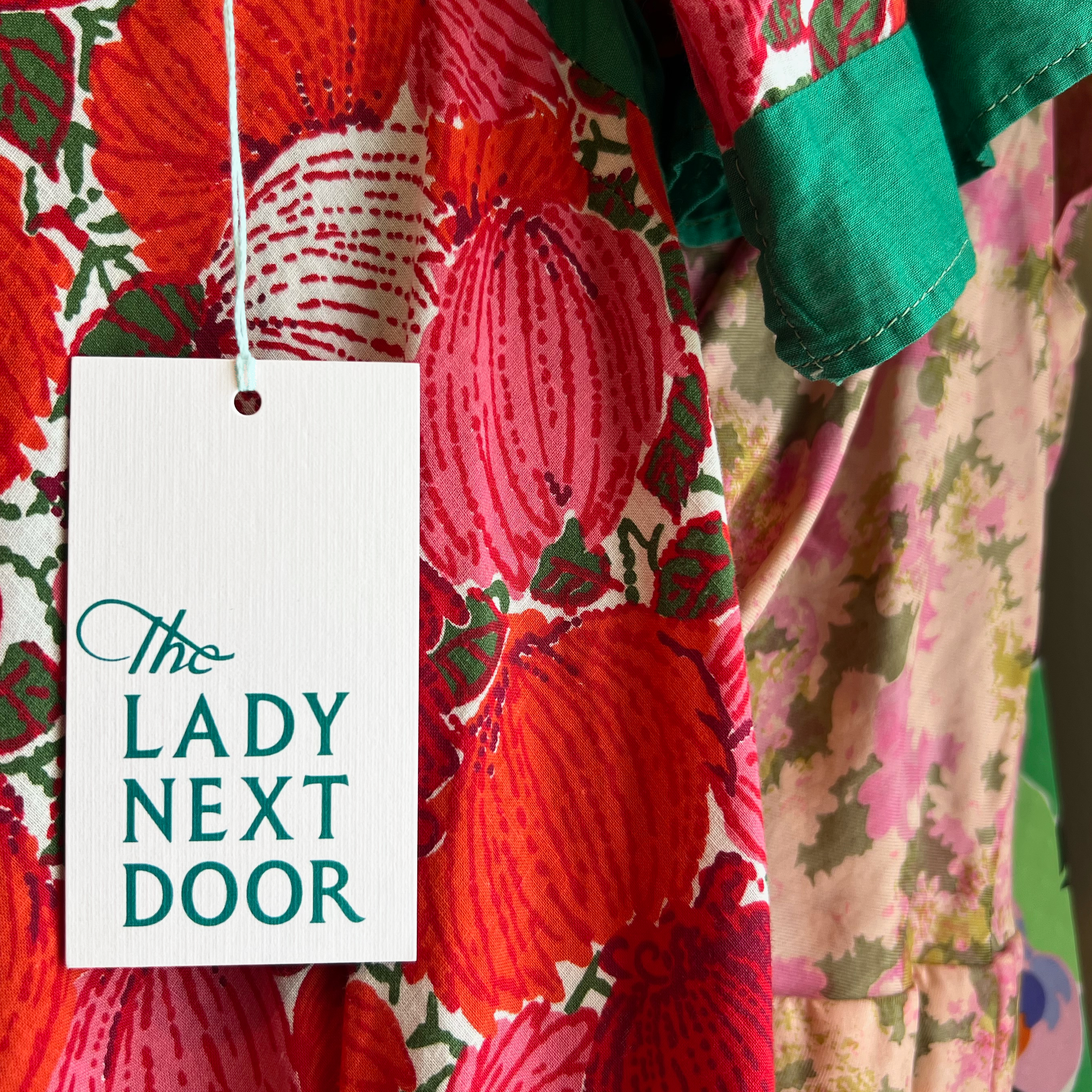 Hangtag that reads "the lady next door" in front of a closeup of vintage clothes
