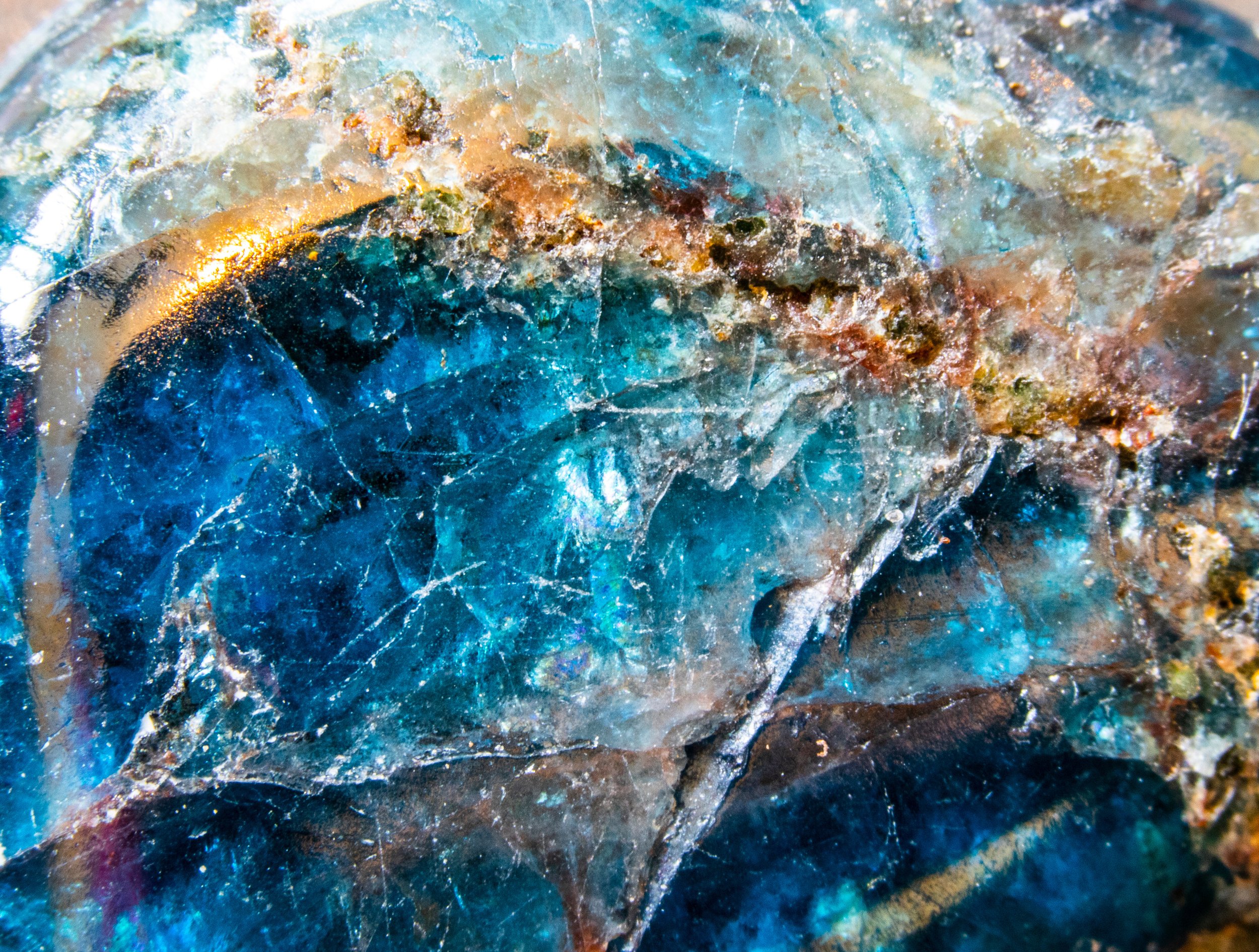 Close-up of a rough, colorful, mineral or gemstone surface with blue, gold, and brown hues, and a textured, crystalline appearance.