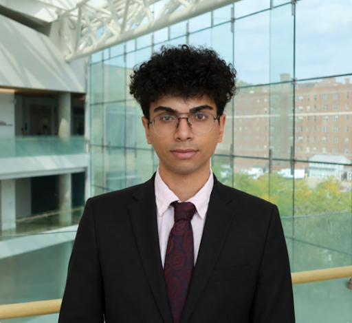 Young man with curly hair and glasses in a suit standing in a modern building with large glass windows