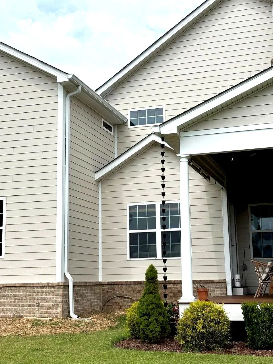 Exterior view of a custom home addition in Chattanooga TN with Hardie board siding, brick foundation, and covered porch with rain chain detail.