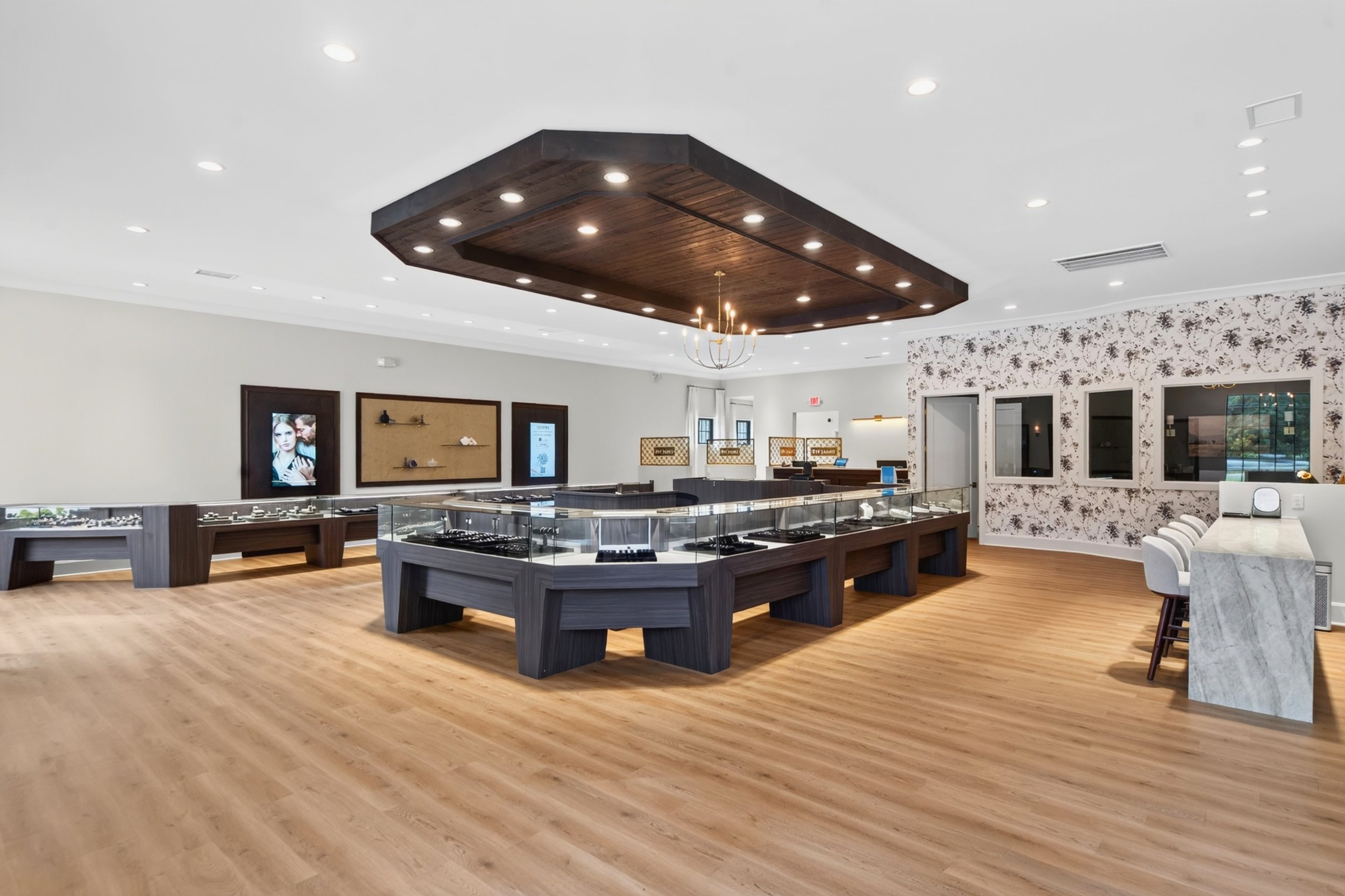 Custom jewelry showroom in Cleveland, TN, featuring glass display cases, LVP flooring, extensive recessed lighting, an elegant chandelier, and a dramatic wood-paneled ceiling feature, designed and built by local commercial builder VMH Construction.
