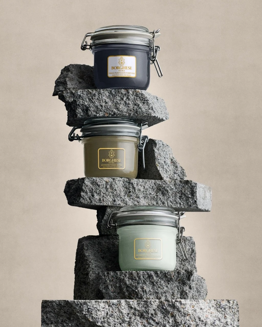 Three small jars of Borghese face and body mud placed on stacked stones, each jar has a different color.