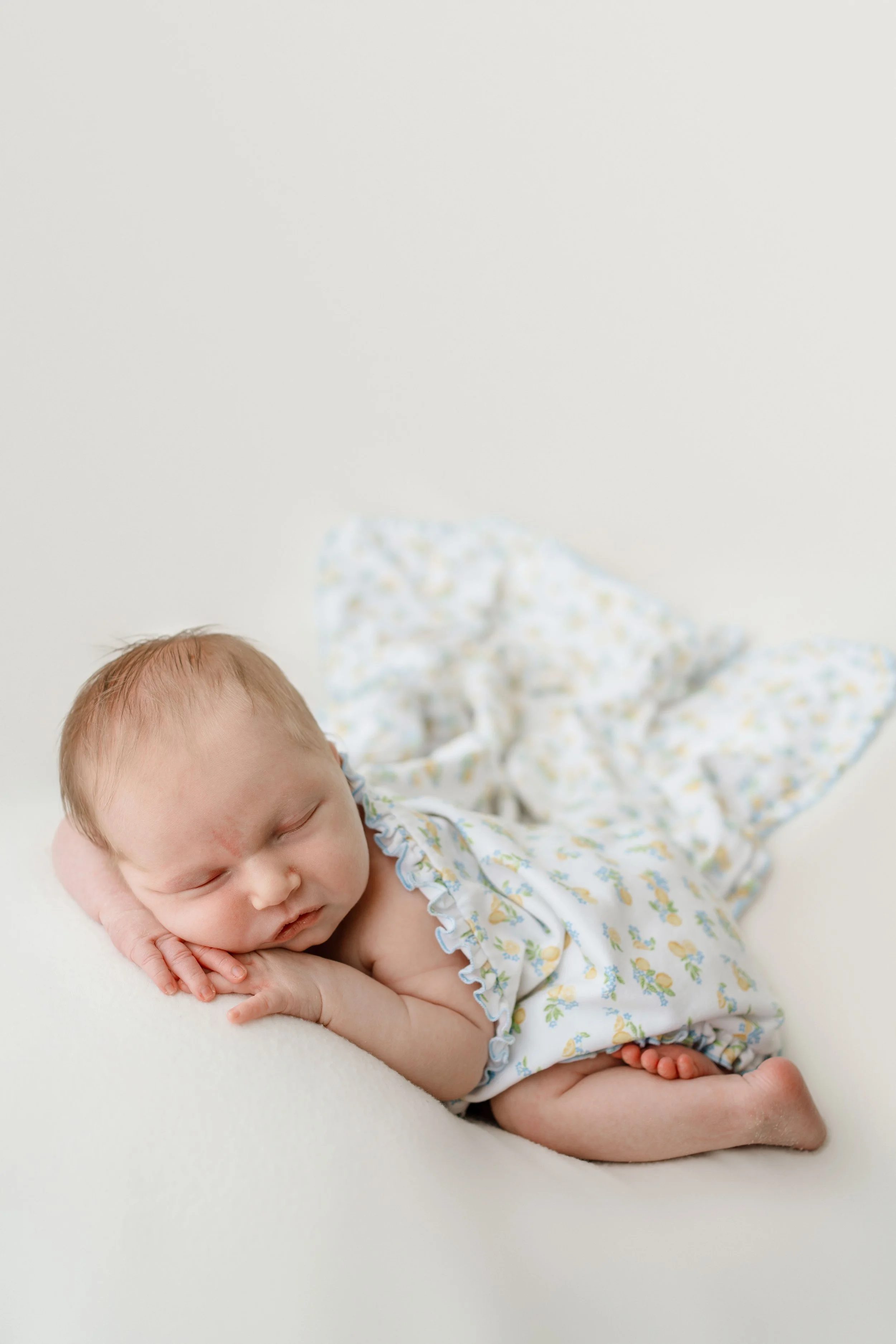 newborn posed baby laying on side with her little fingers showing under her cheeks with studio lighting
