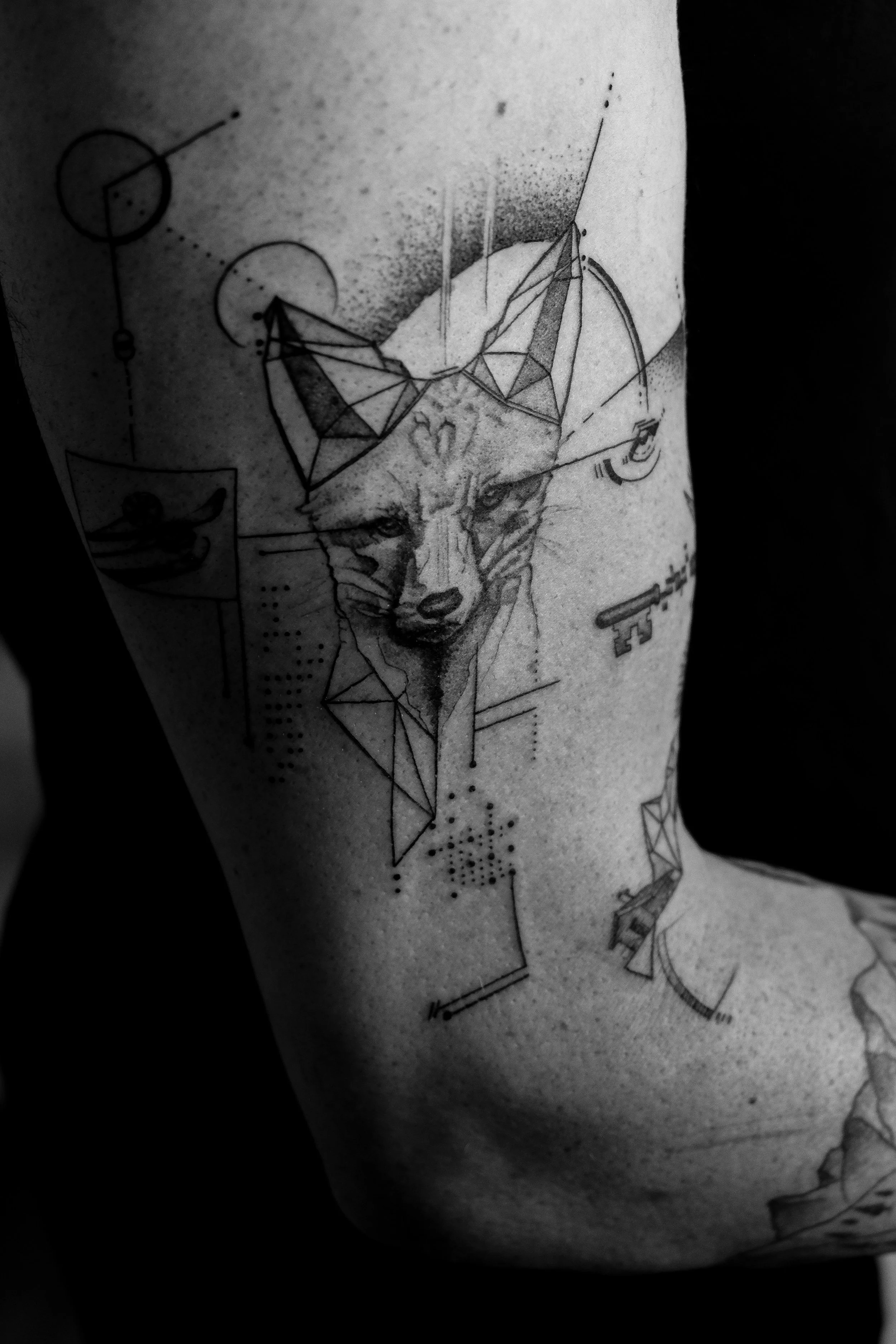 Schwarze Tätowierung eines Wolfsgesichts mit geometrischen Elementen auf einem Oberarm.