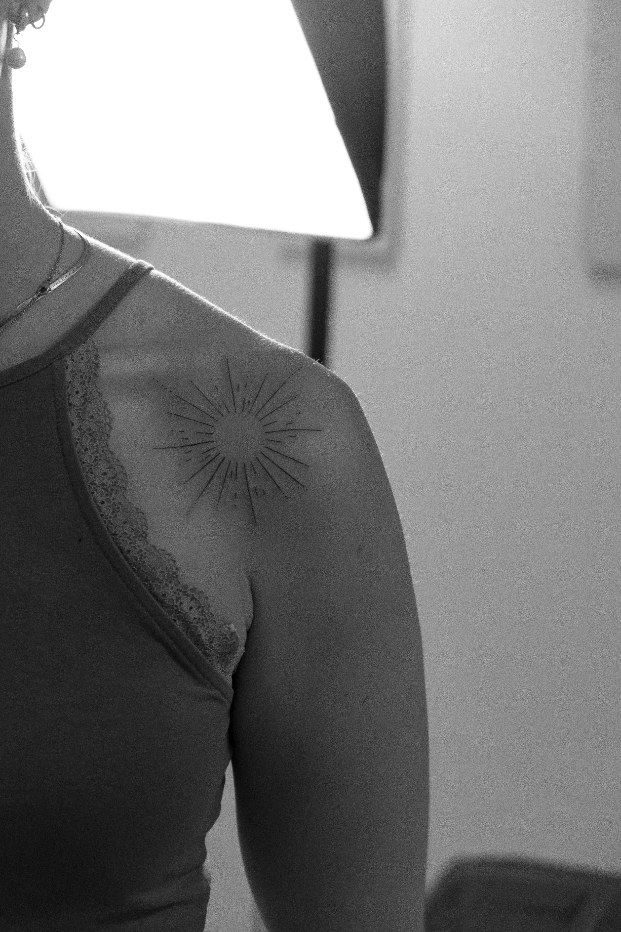 Schwarz-weiße Aufnahme eines Menschen, der über die Schulter fotografiert wurde, mit einer Sonnen-Tattoo auf der Schulter.
