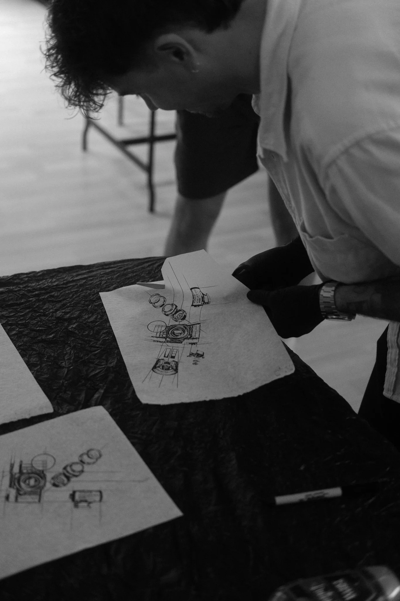 Ein Mann betrachtet technische Zeichnungen auf Papier auf einem Tisch, schwarz-weiße Aufnahme.