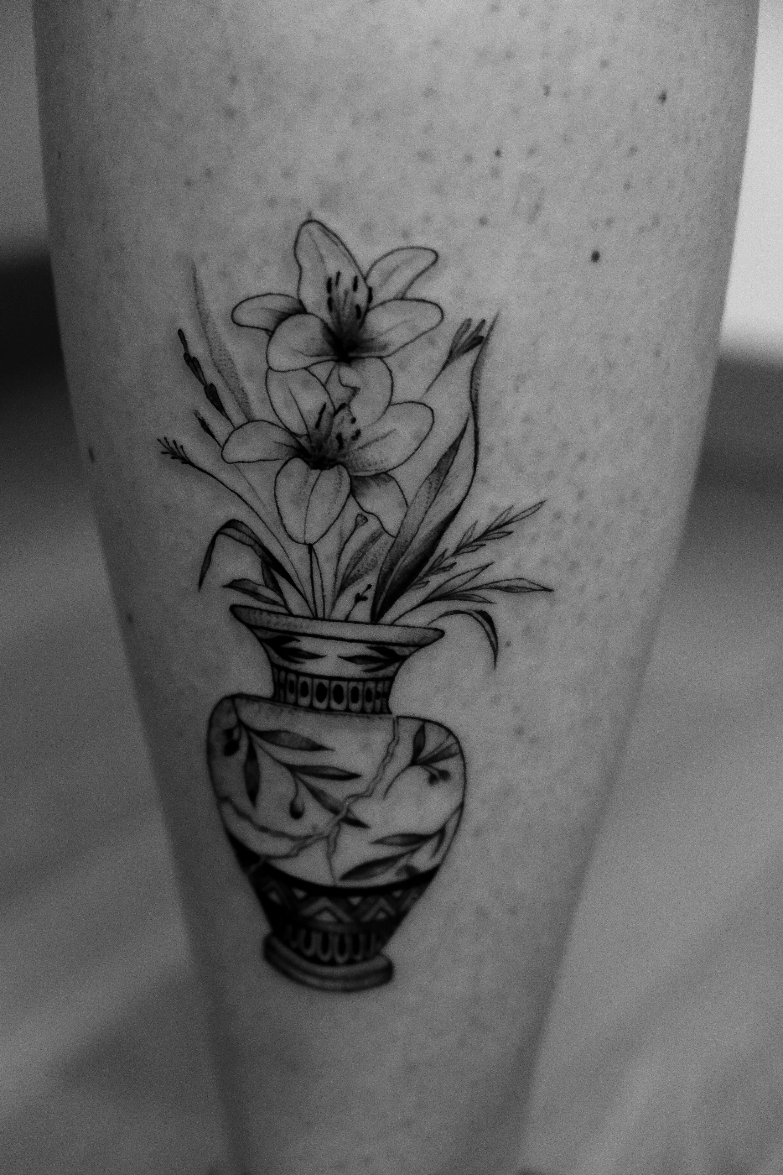 Schwarze Tätowierung eines Blumentopfs mit Blumen auf menschlicher Haut.