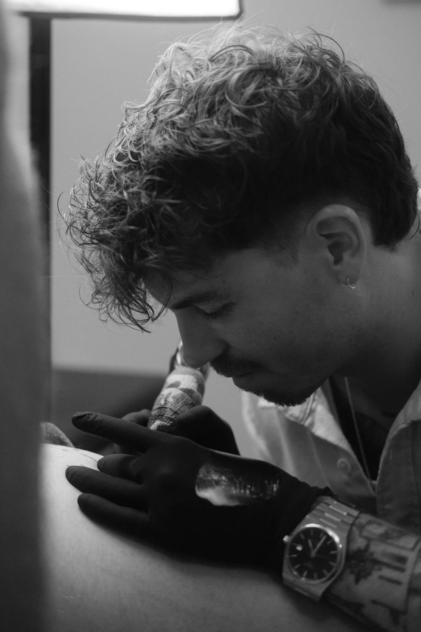 Tattoo-Künstler beim Tätowieren einer Person im Tattoo-Studio Sketchy Riedi, in Schwarz-Weiß-Foto.