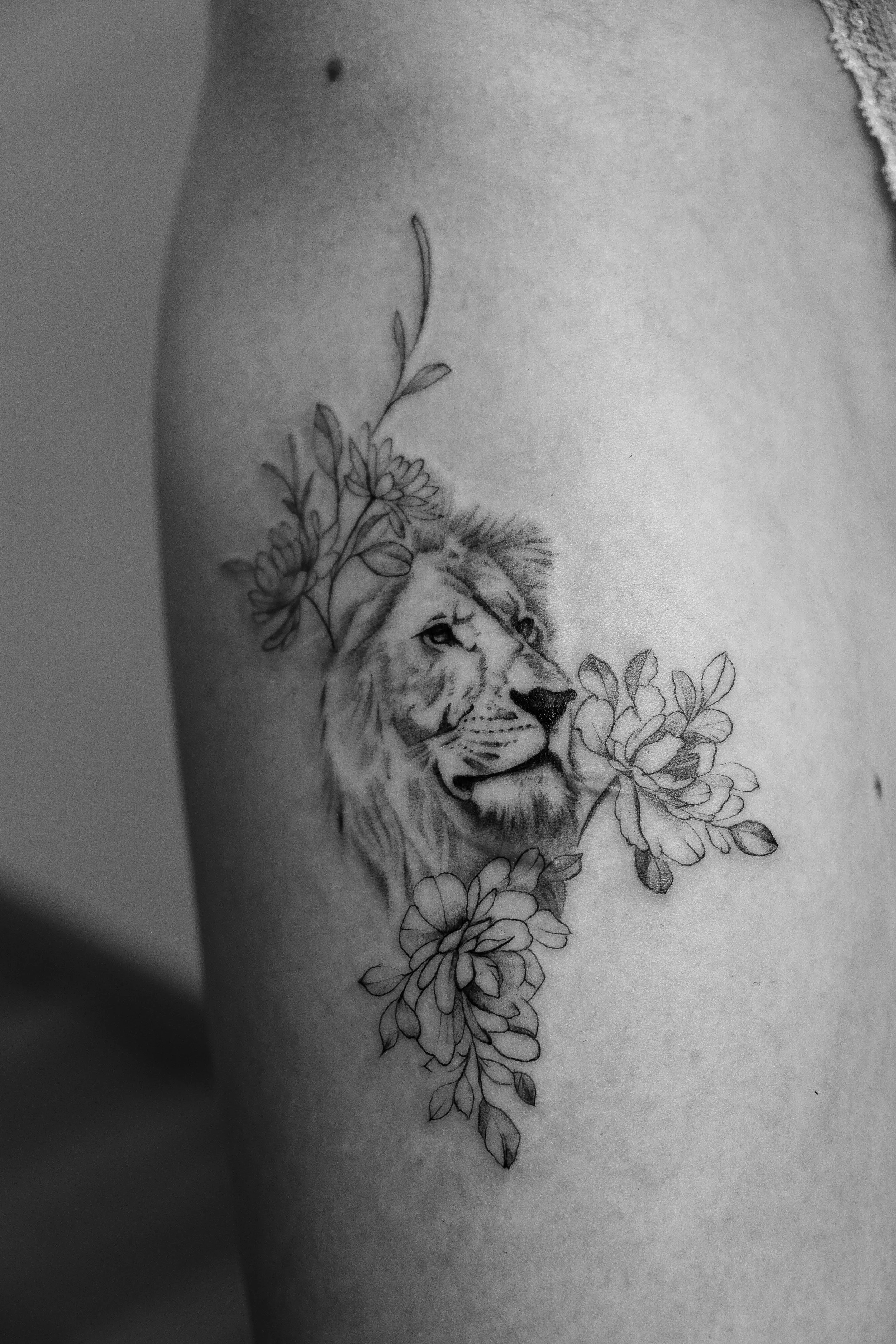 Schwarze Tätowierung eines Löwenkopfes mit Blumen und Blättern auf der Haut.