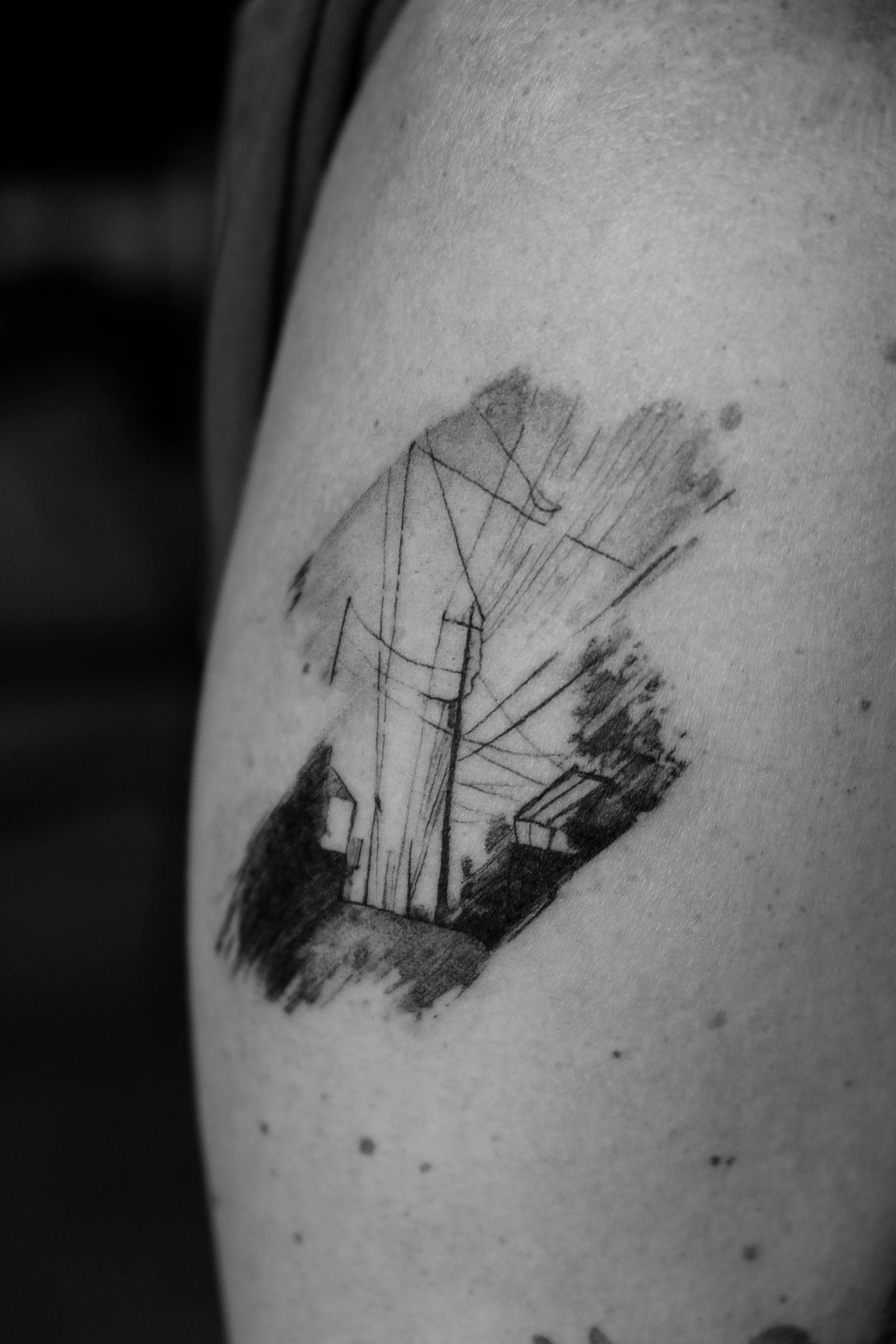 Schwarze Tätowierung zeigt ein Haus und eine Stromleitung auf der Haut, in Schwarz-Weiß-Optik.