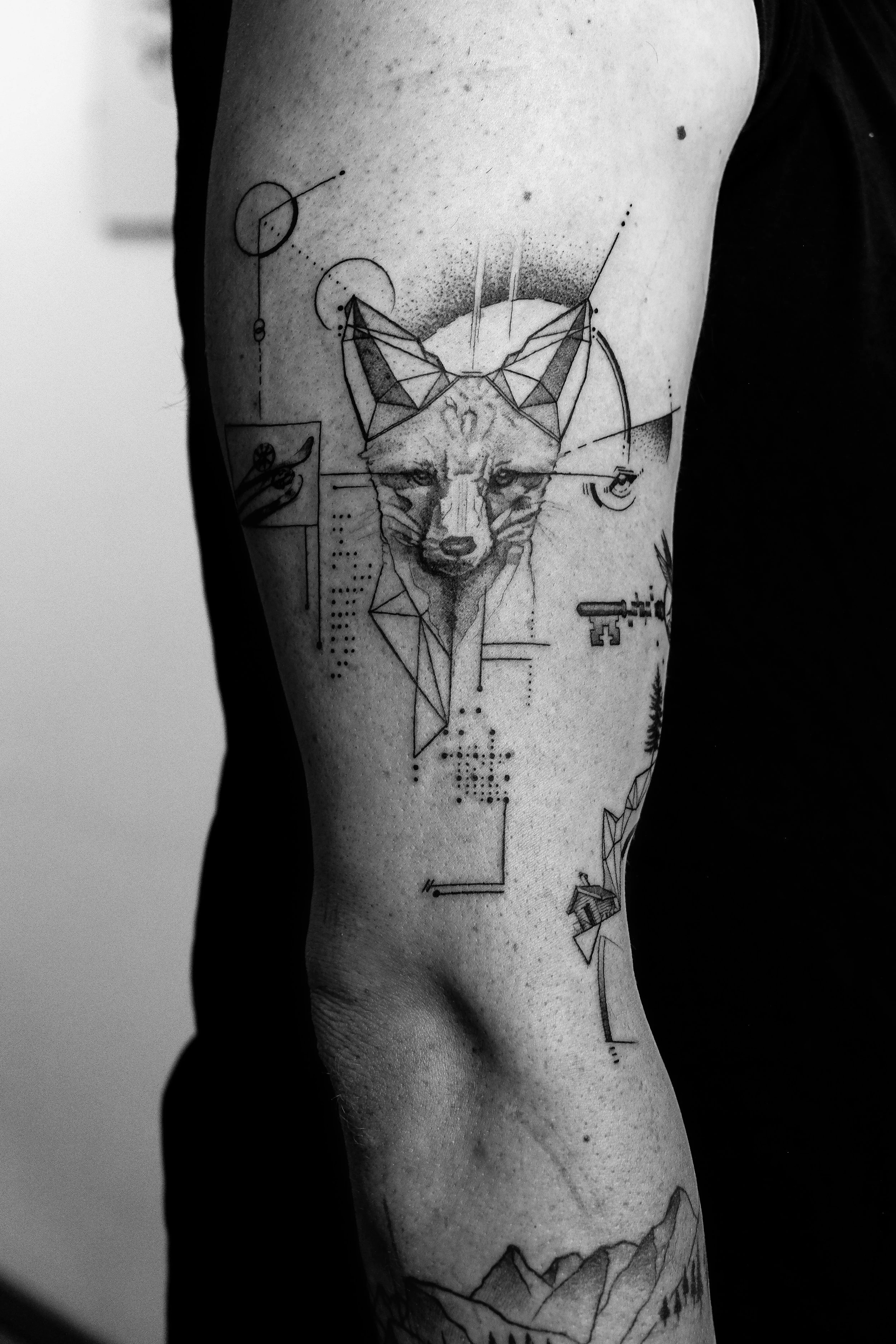 Schwarze und graue Tätowierung eines Wolfsgesichts mit geometrischen und technischen Elementen auf einem menschlichen Oberarm.