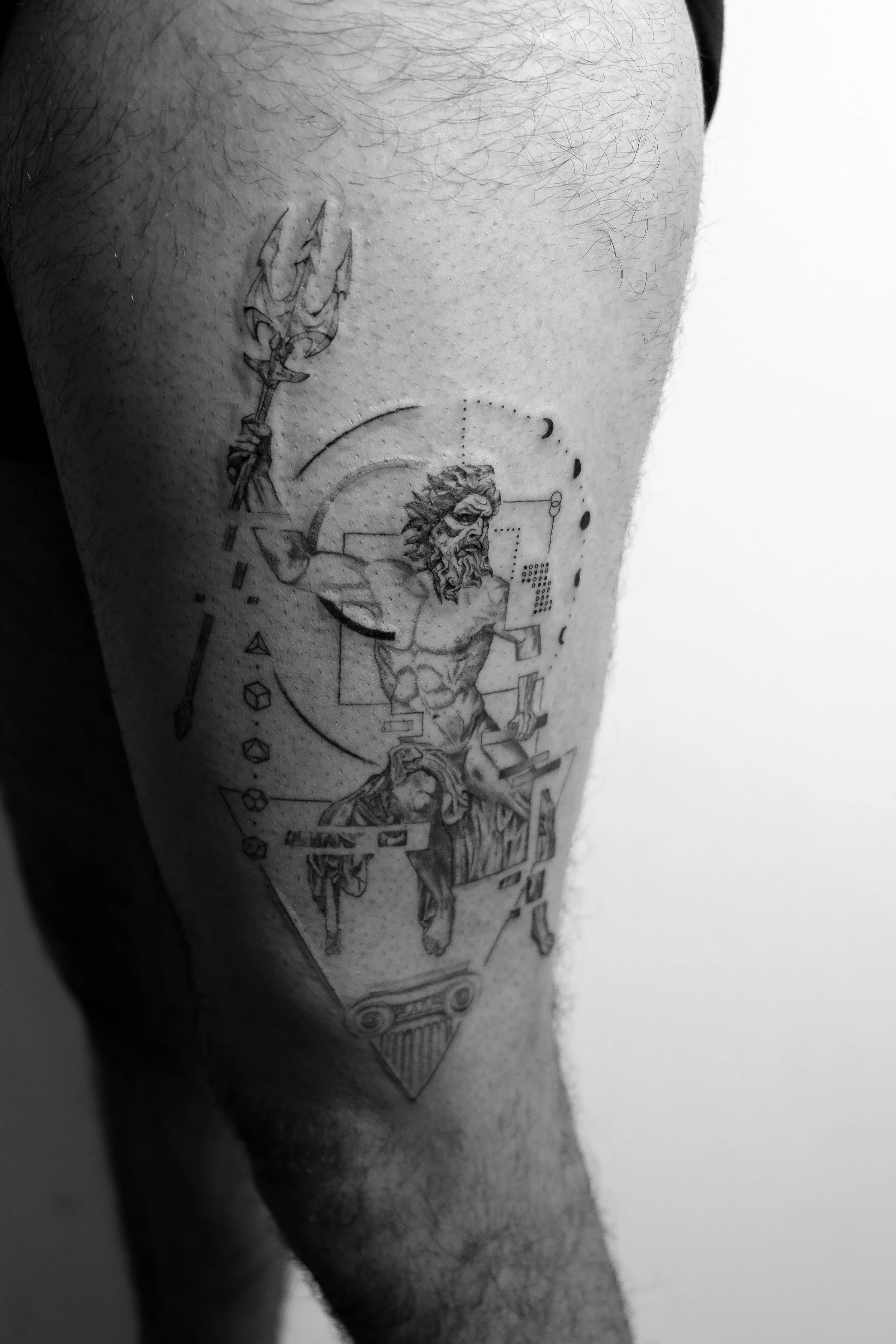 Schwarze Tätowierung eines religiösen Motivs mit Jesus auf einem Kreuz, geometrischen Formen und wissenschaftlichen Symbolen auf einem menschlichen Oberschenkel.