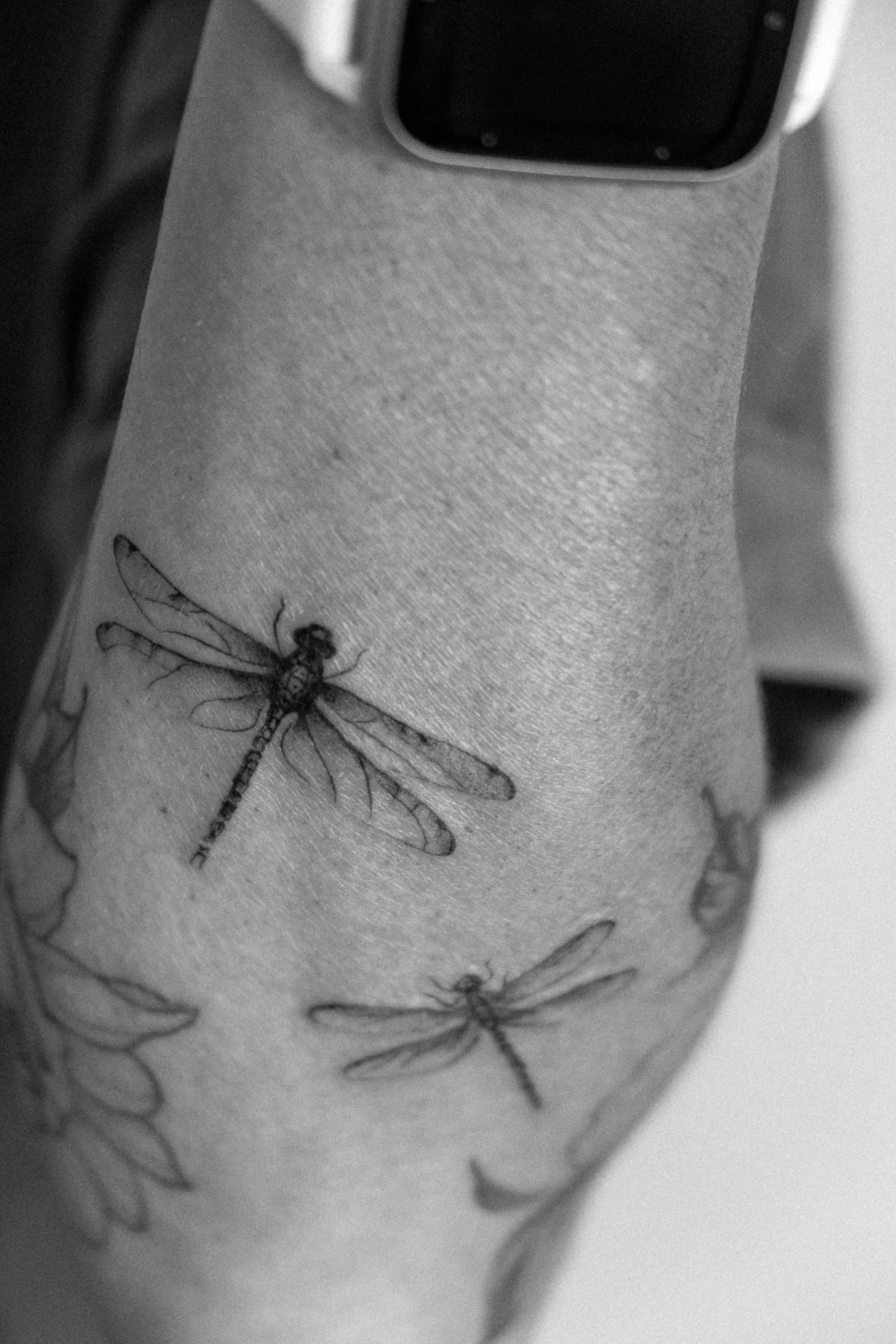 Schwarze Tattoos von Libellen auf dem Unterarm in Schwarz-Weiß.