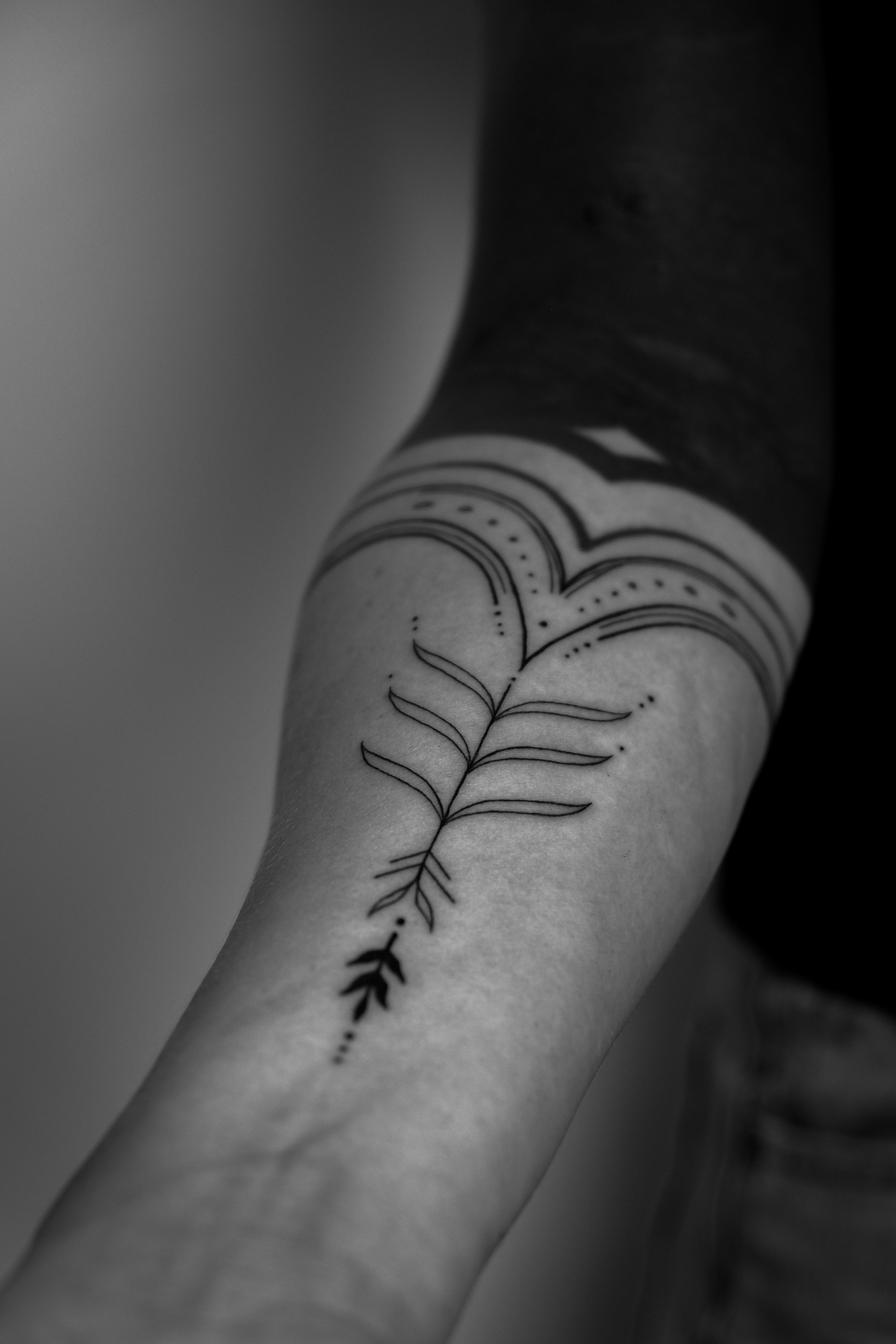 Schwarze und weiße Tattoo eines Zweigs mit Blättern auf dem Unterarm.