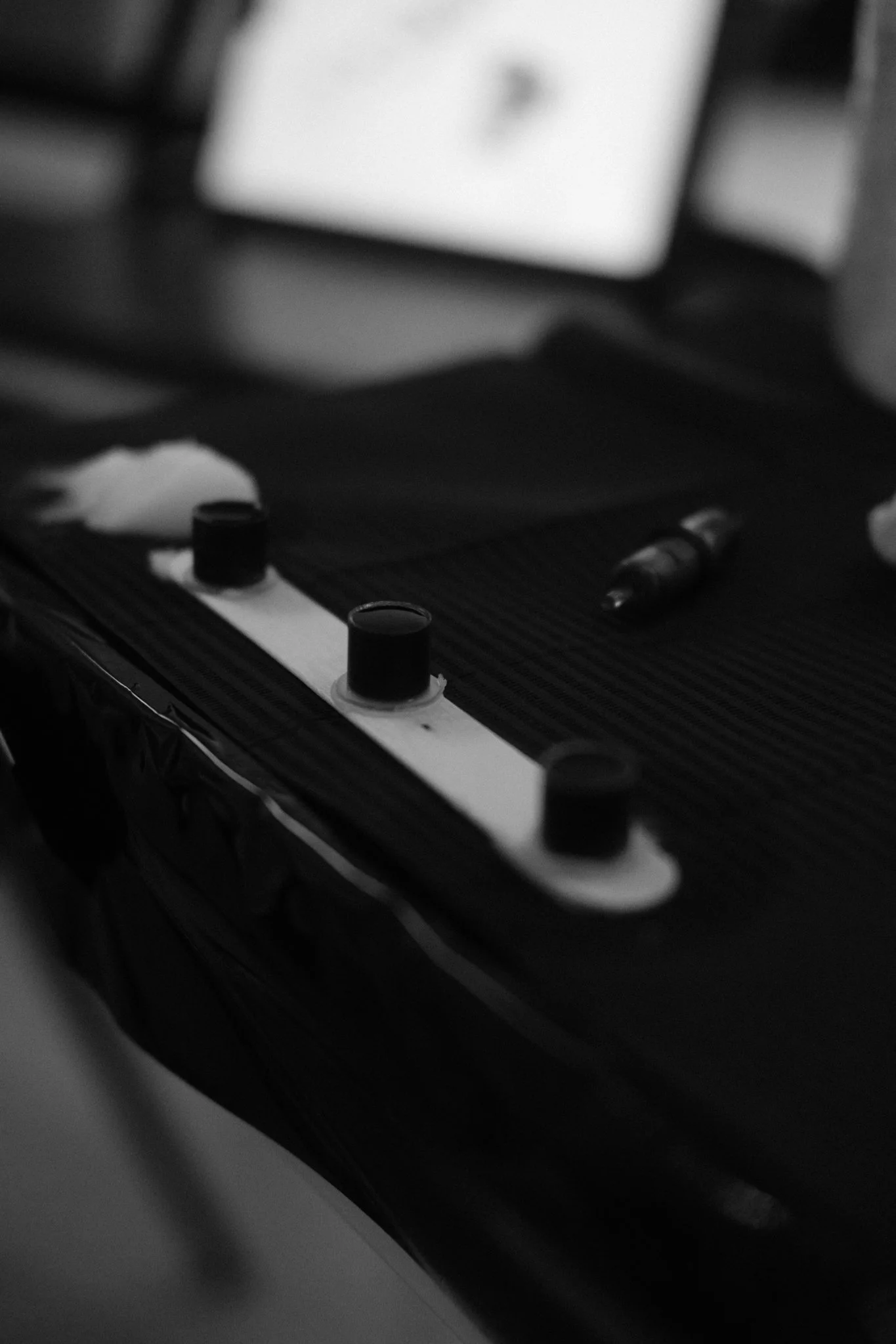 Schwarz-weiß-Foto eines Tischs mit elektronischen Komponenten, darunter zwei runde Knöpfe, eine kleine Tintenpatrone, ein Marker und eine mehrspurige Leiterplatte.