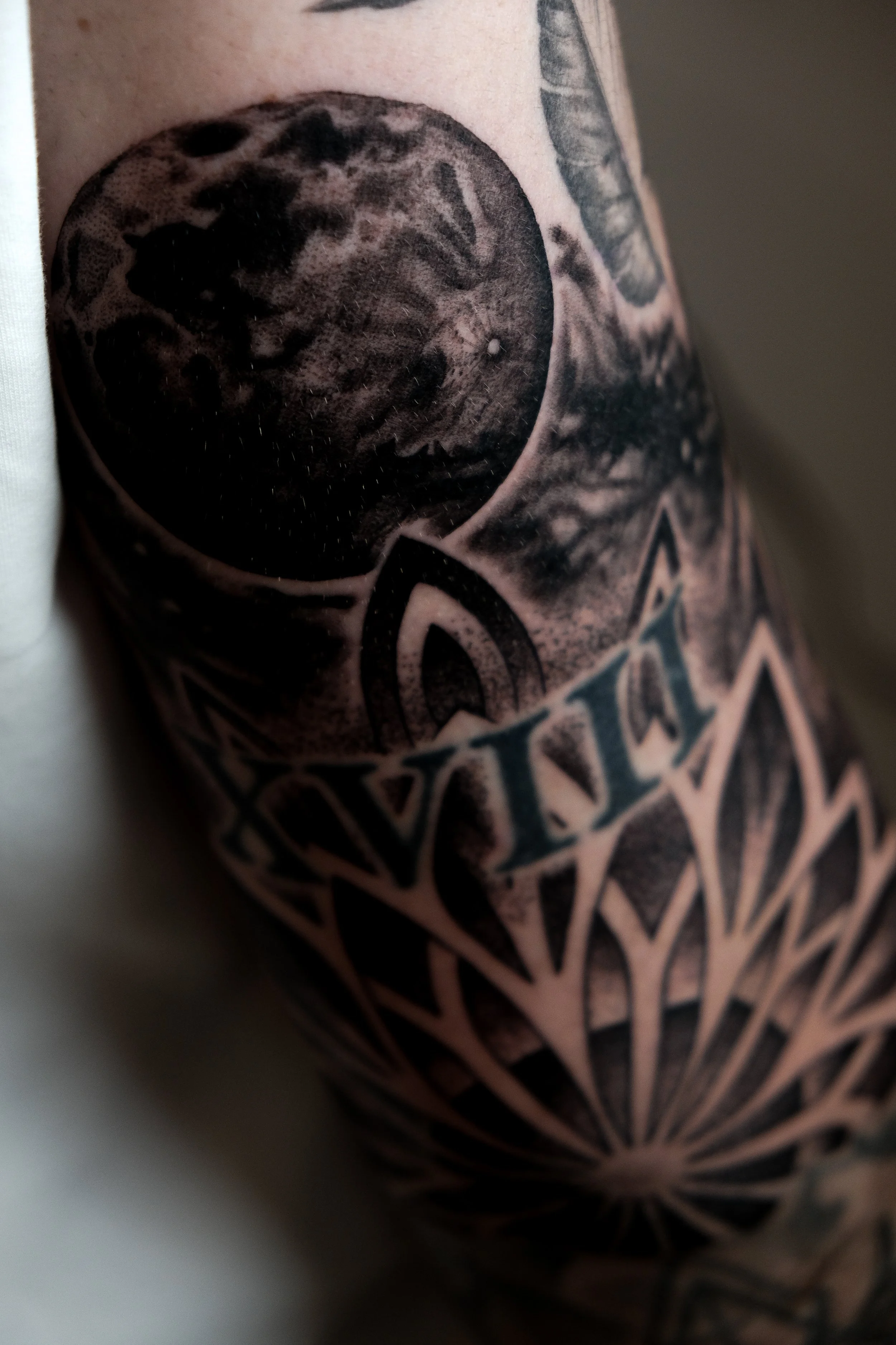 Nahaufnahme eines schwarzen Tattoos auf der Haut, das einen Mond und geometrische Muster zeigt.