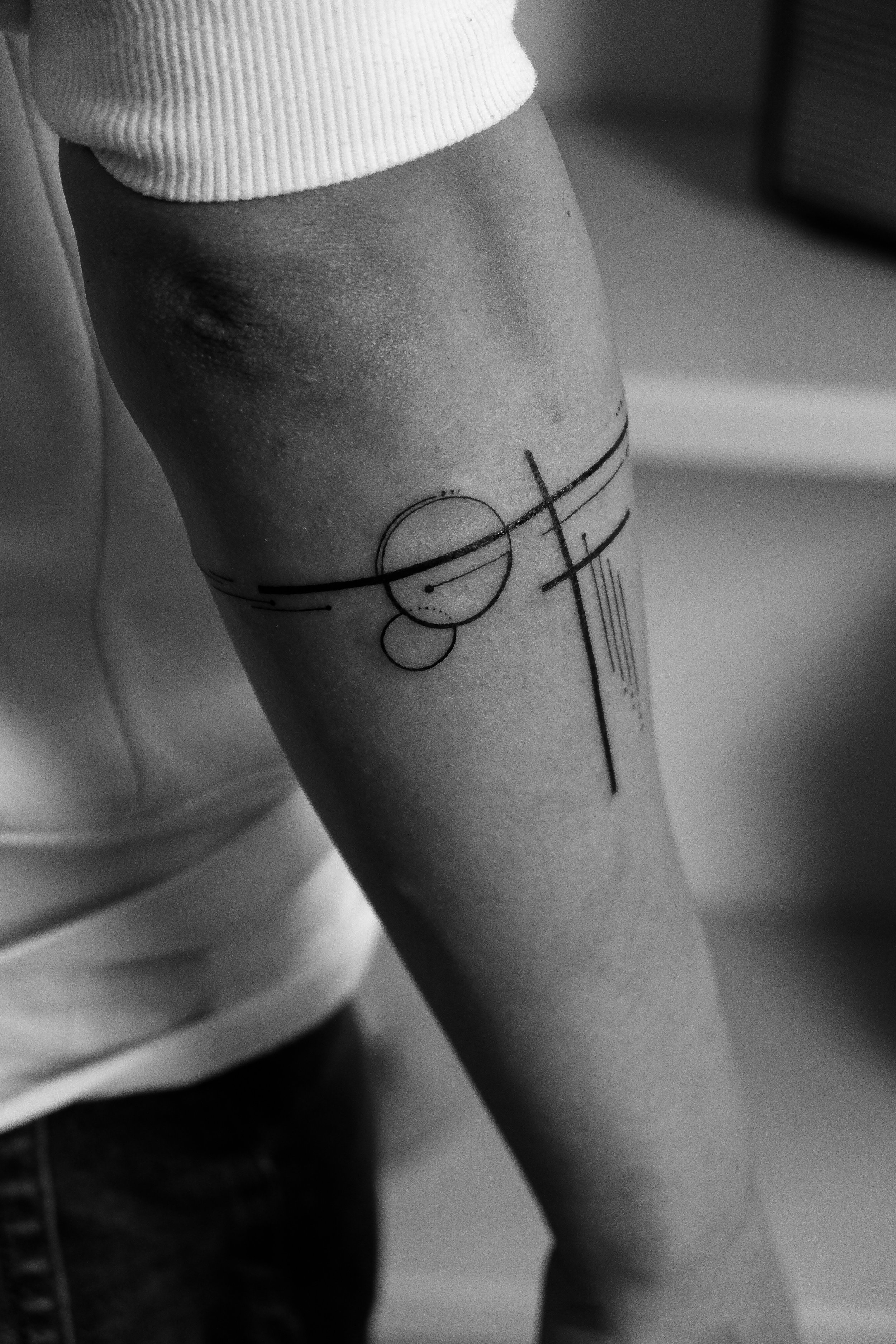 Schwarze Tätowierung mit geometrischen Formen auf dem Oberarm einer Person.