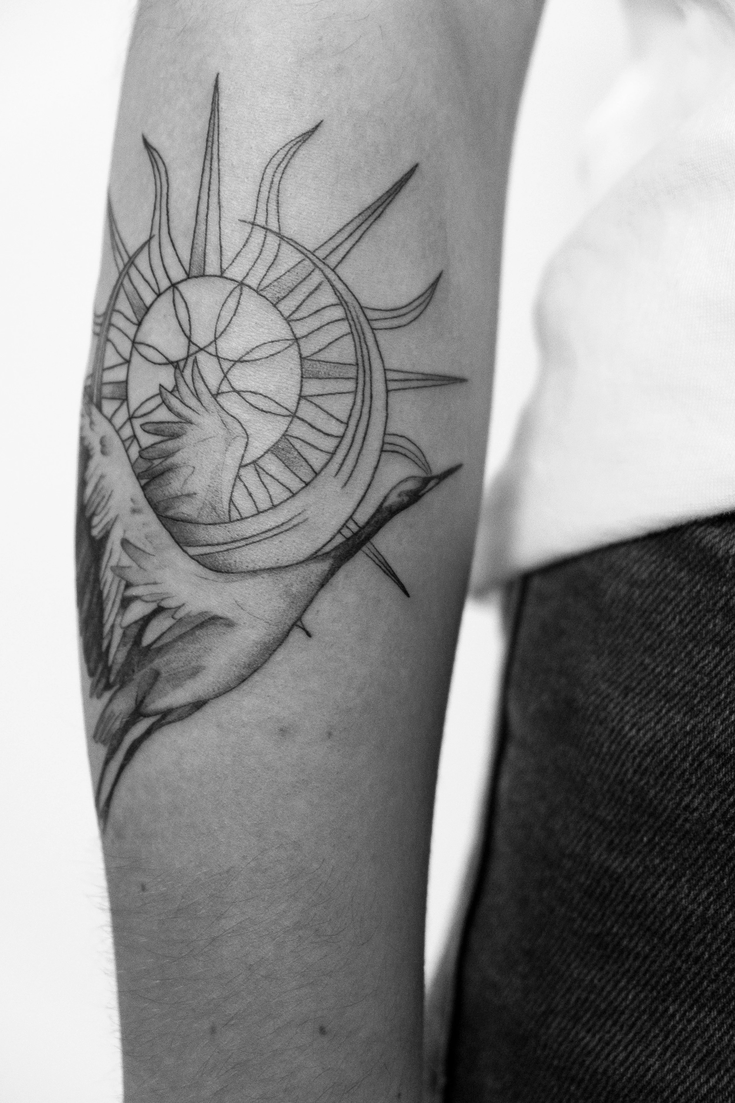 Schwarz-Weiß-Tattoo auf dem Unterarm einer Person, das eine Sonne, einen Mond und eine Hand zeigt, die eine Kristallkugel hält.