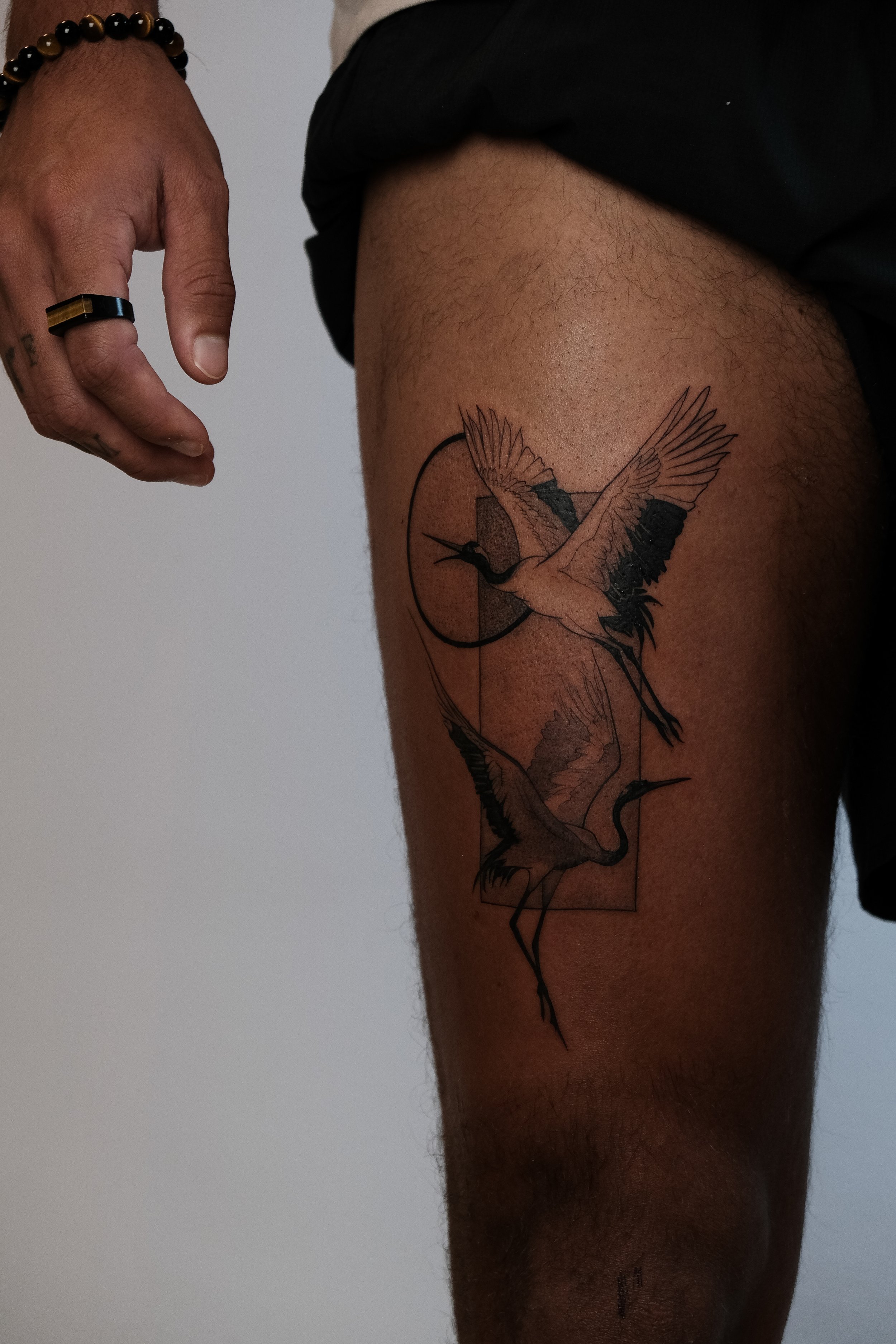 Tattoo eines stehend fliegenden Vögels (vermutlich eine Schwalbe oder ein Kolibri) auf einem Oberschenkel, mit geometrischem Design und einem Kreis im Hintergrund.