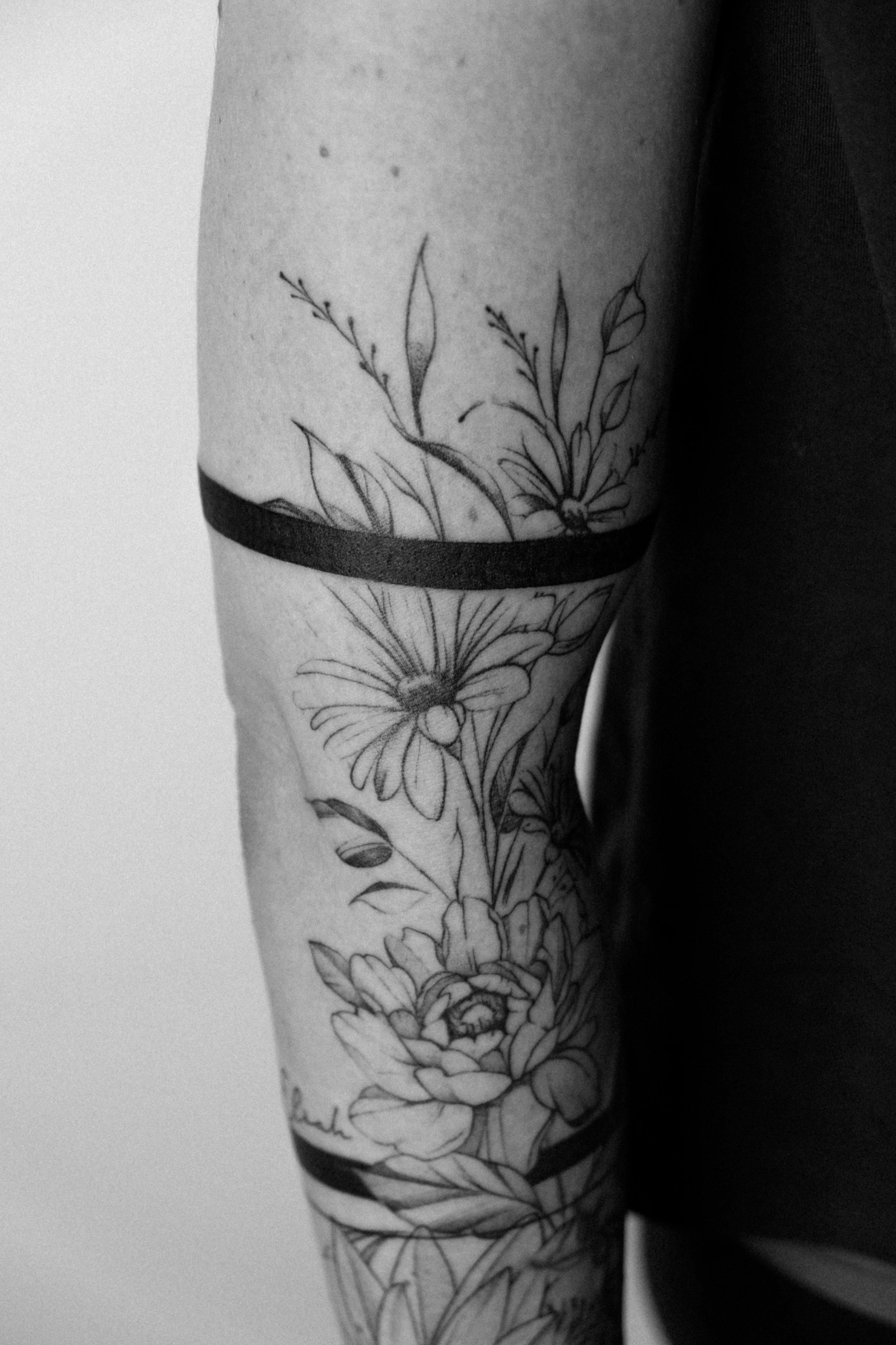 Schwarz-weiße Tätowierung eines Blumenmusters auf einem Arm, inklusive verschiedener Blüten und Blätter.