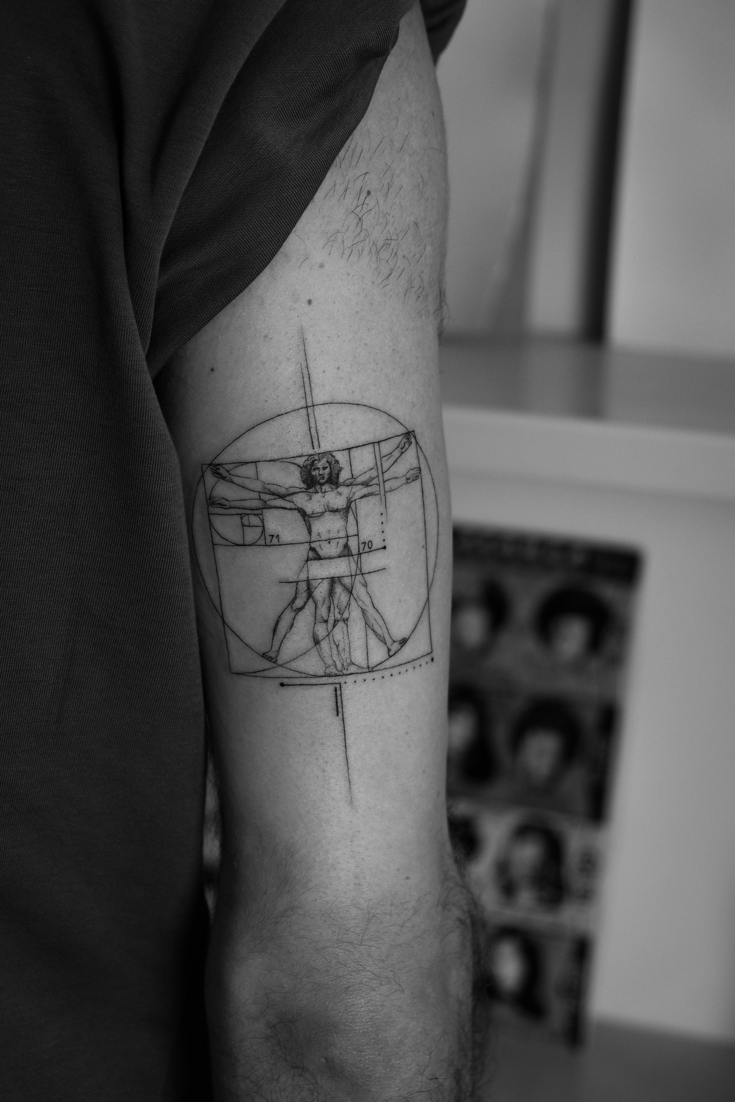 Schwarz-weiß-Tattoo eines geometrisch inspirierten Leonardo da Vinci's Vitruvianischen Menschen auf einem Oberarm.