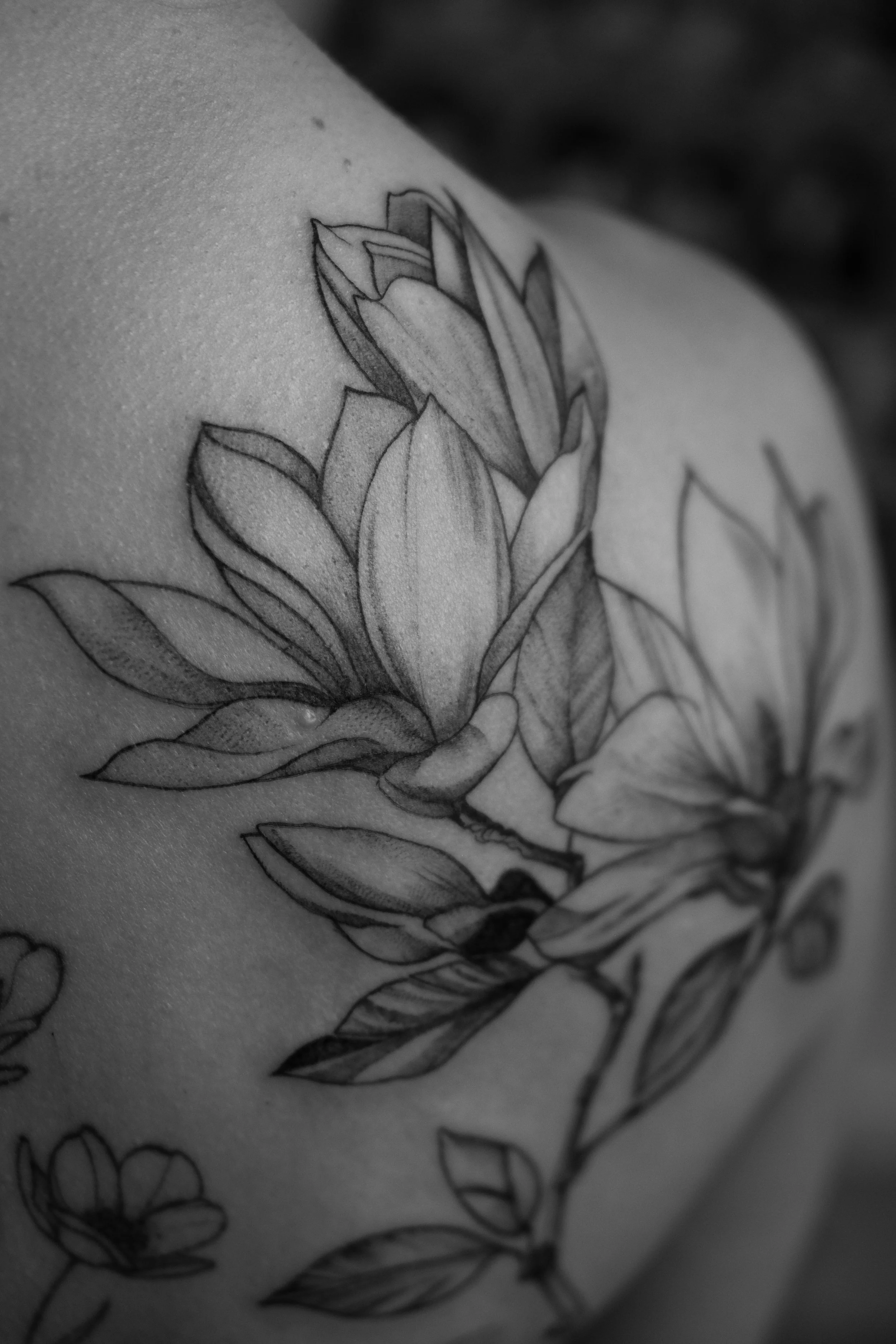 Schwarz-weiß-Tattoo einer Blume mit Blättern auf der Haut.