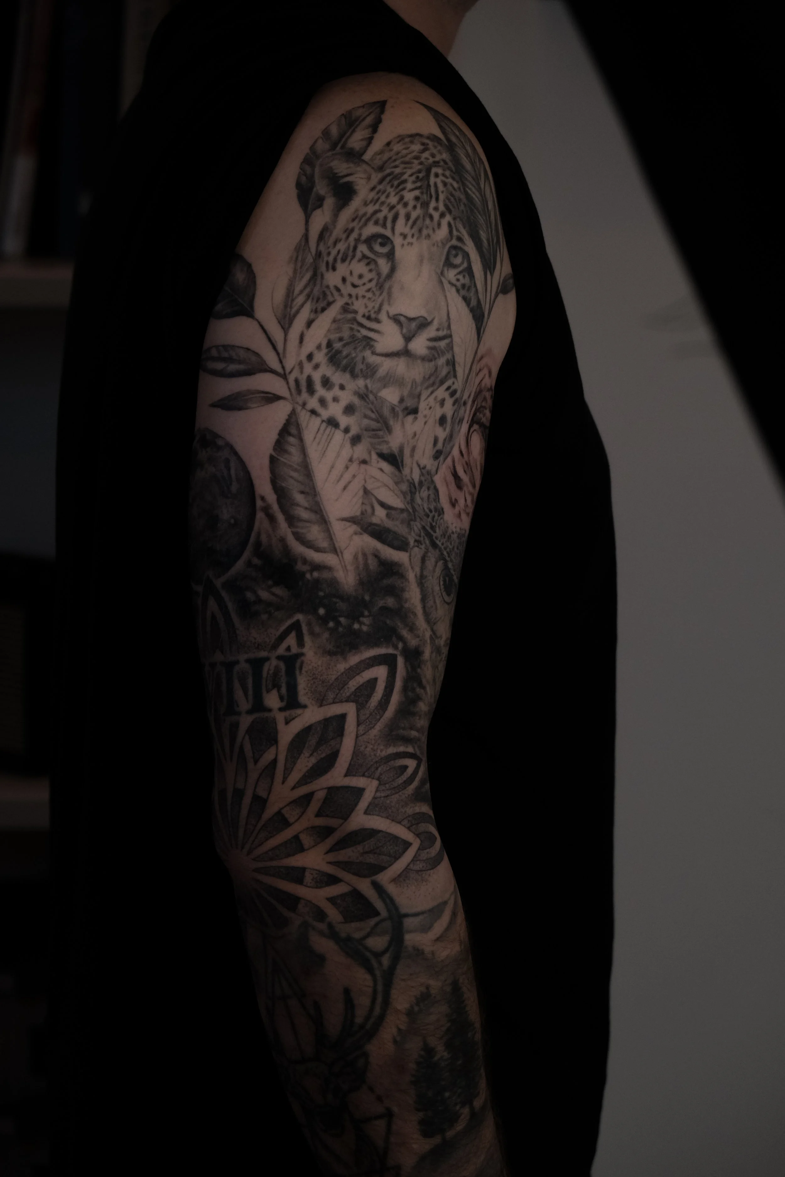 Tattoo eines Leopardenkopfes mit Blättern, Blumen und anderen Tieren auf dem Oberarm einer Person.